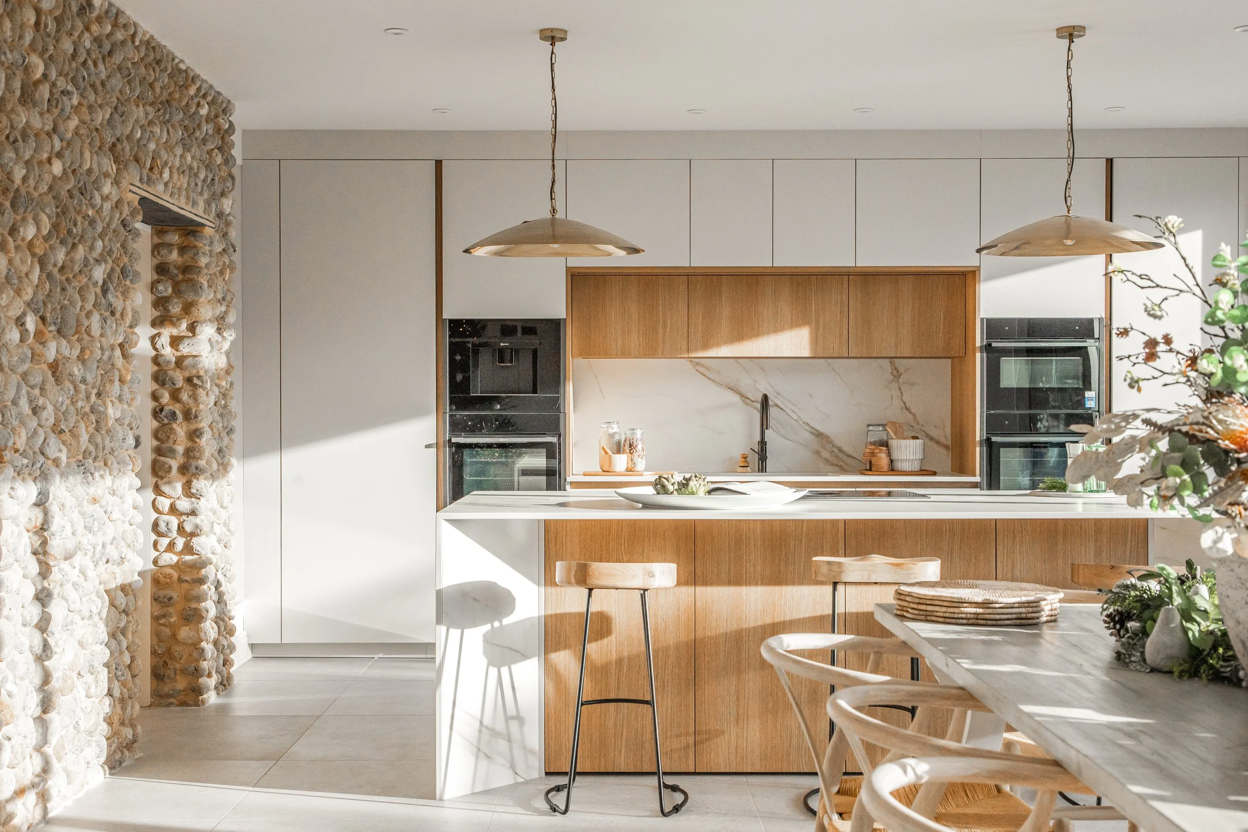 Modern kitchen with white cabinetry, wooden accents, stone wall, and hanging pendant lights.