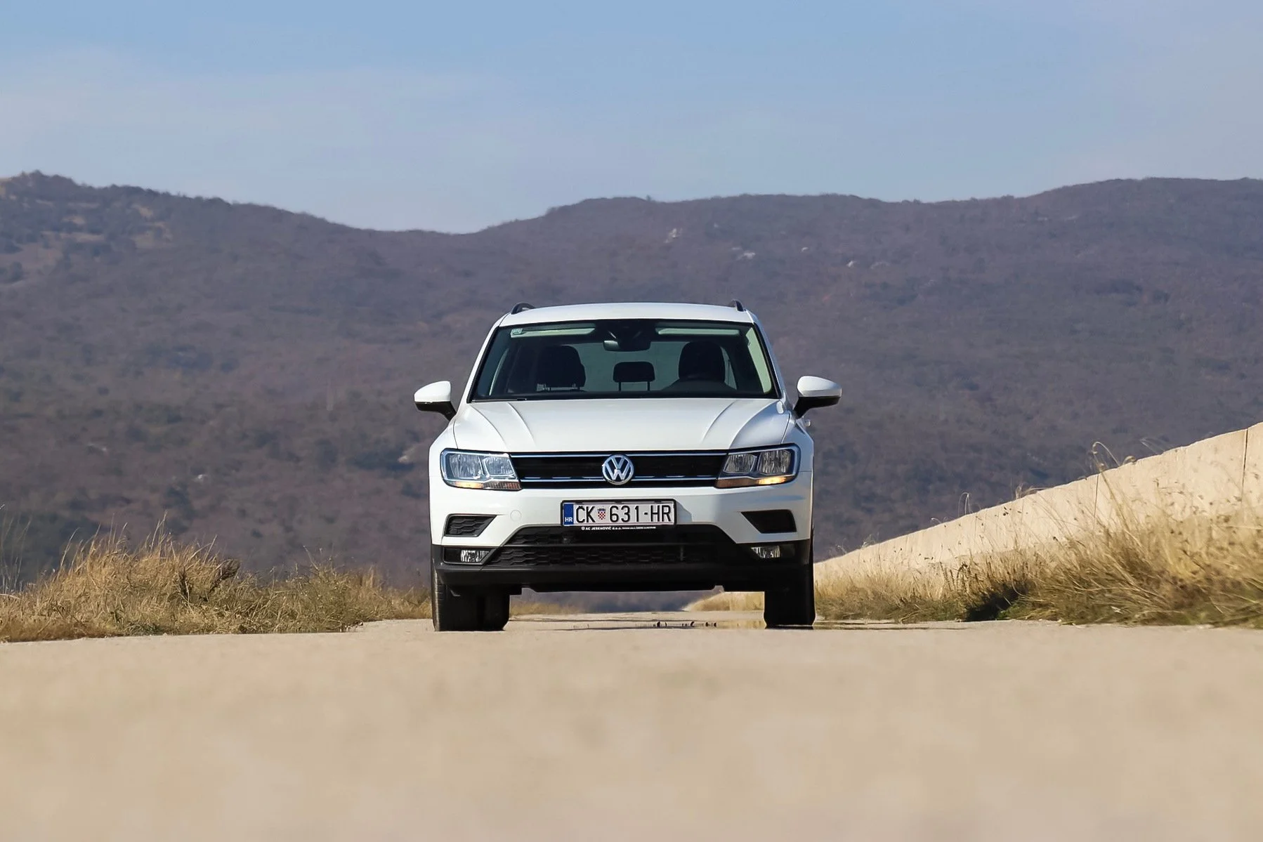 A white Volkswagen SUV driving on an open road with hills in the background under a clear blue sky.