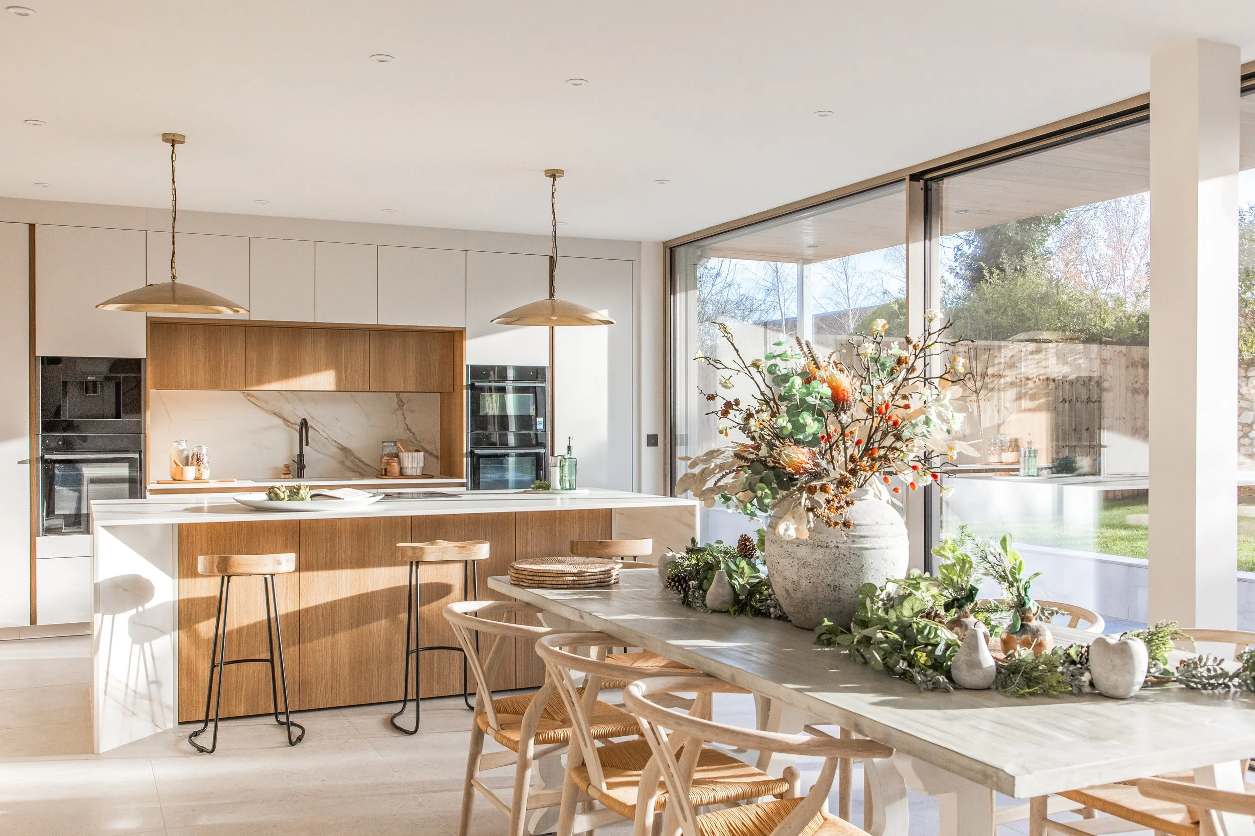 A modern kitchen with a white and wood island, pendant lights, and a large table decorated with a centerpiece of flowers and greenery.