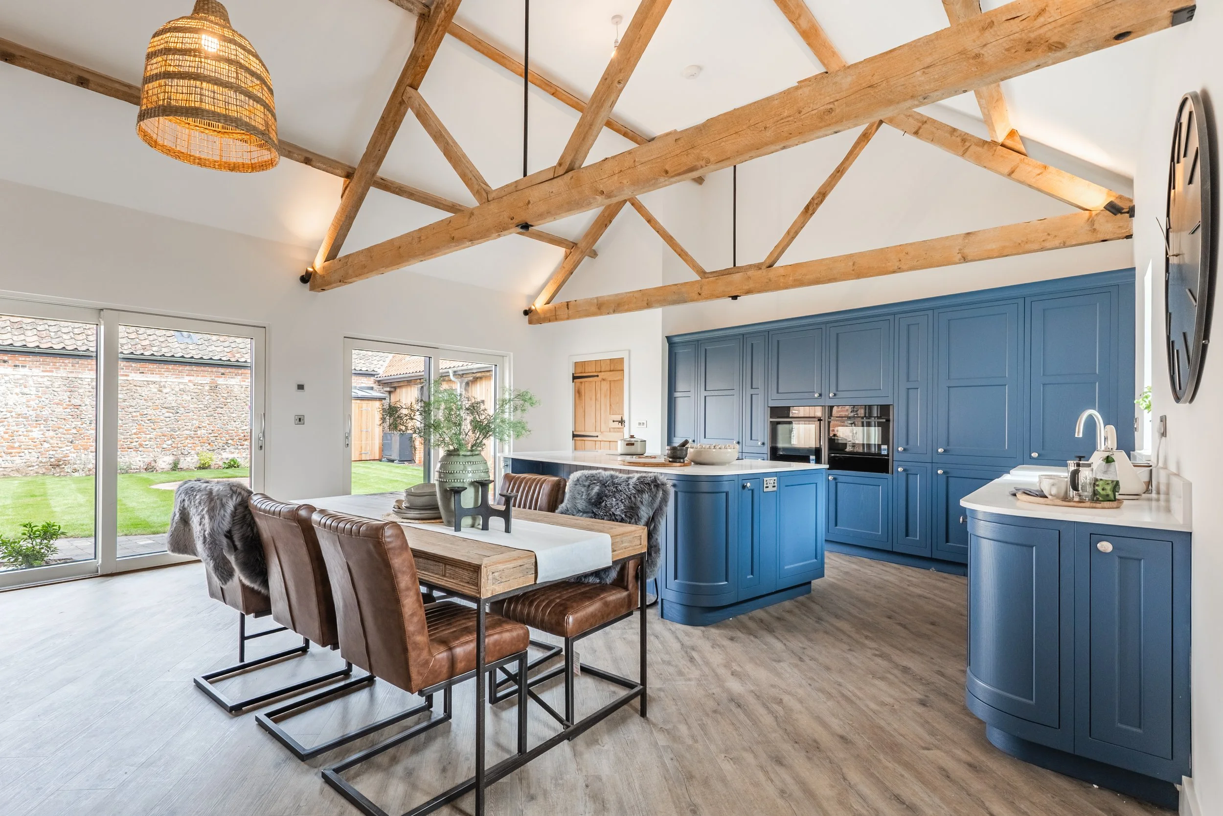 Open-concept kitchen and dining area with exposed wooden beams, blue cabinets, and sliding glass doors with outdoor view.