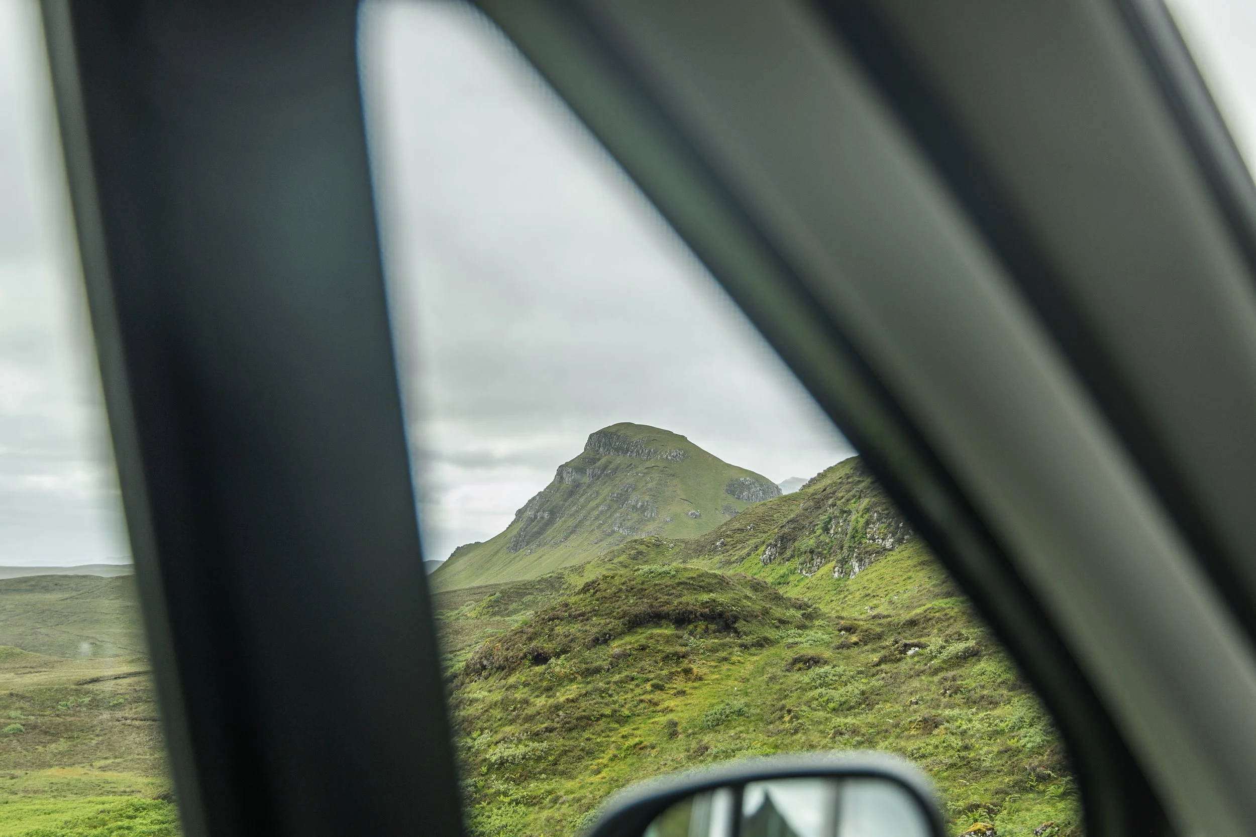 Mountains and green landscape seen through the rearview mirror of a car.