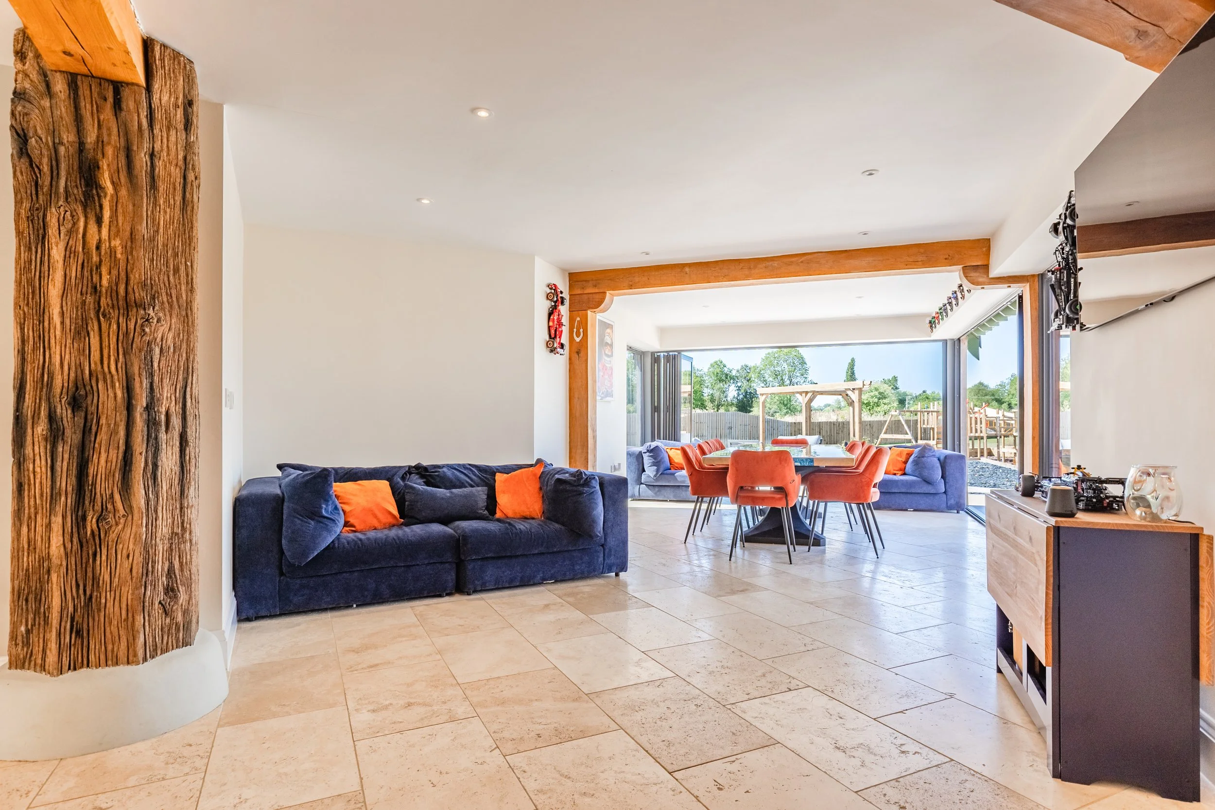 Living room with a navy blue couch and orange pillows, a dining table with orange chairs, large sliding glass doors leading to a backyard, and decorated walls.