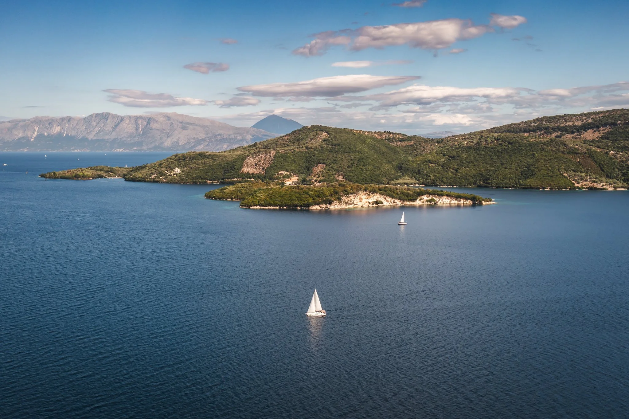 A scenic view of a body of water with sailboats, green islands, and distant mountains under a partly cloudy sky.