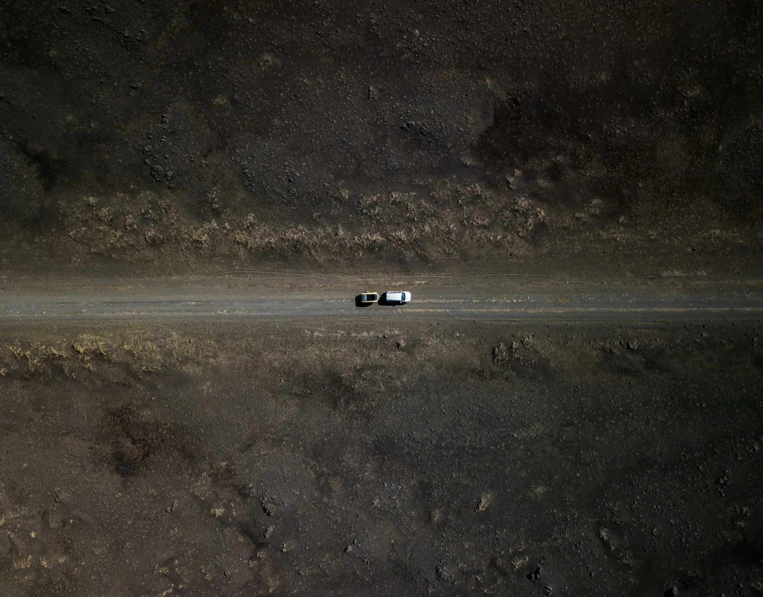 An aerial view of two vehicles parked on a dirt road in a barren, rocky landscape.