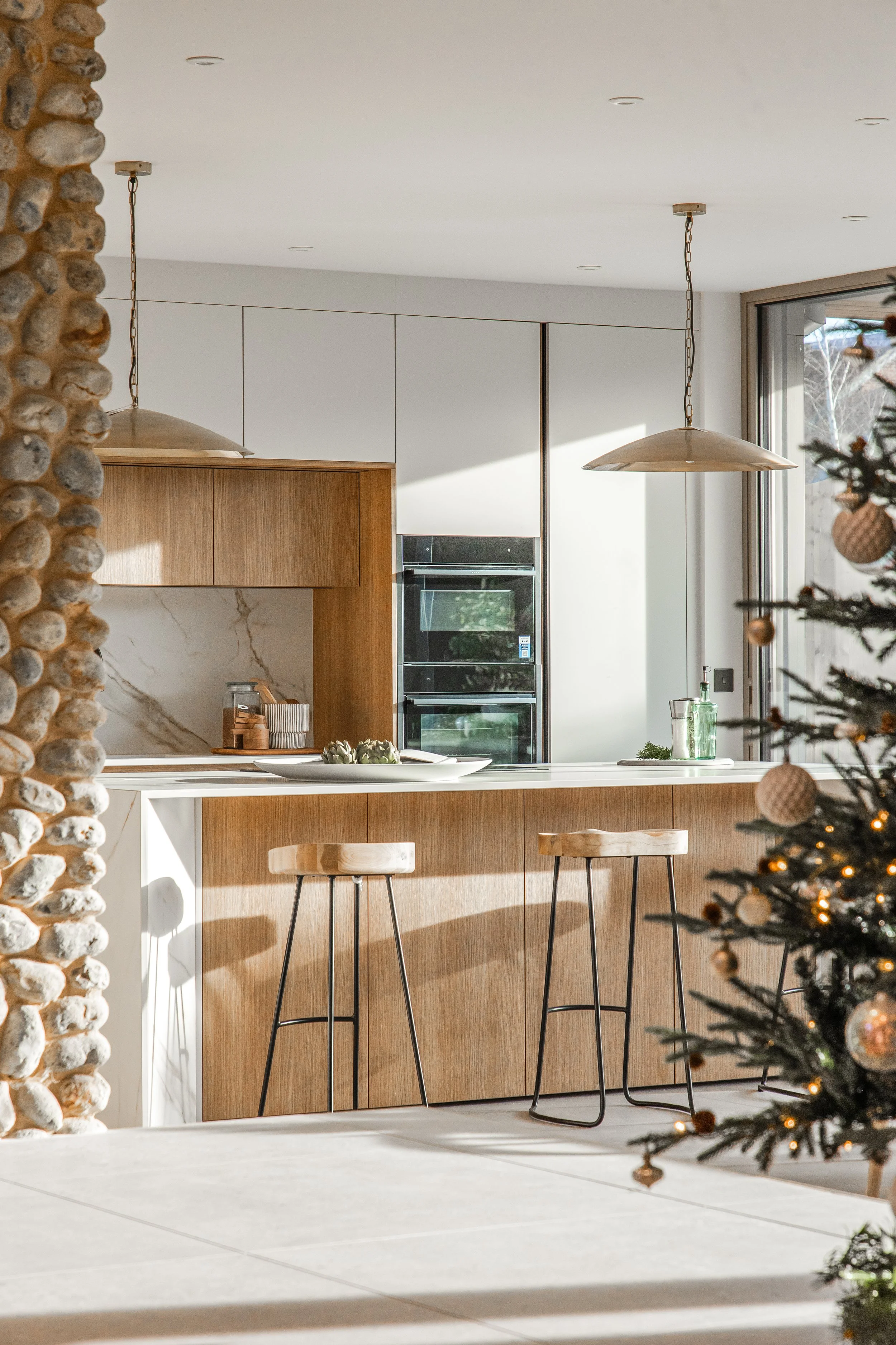 Modern kitchen with white cabinetry, wooden accents, and black appliances, decorated for Christmas with a Christmas tree in the foreground.