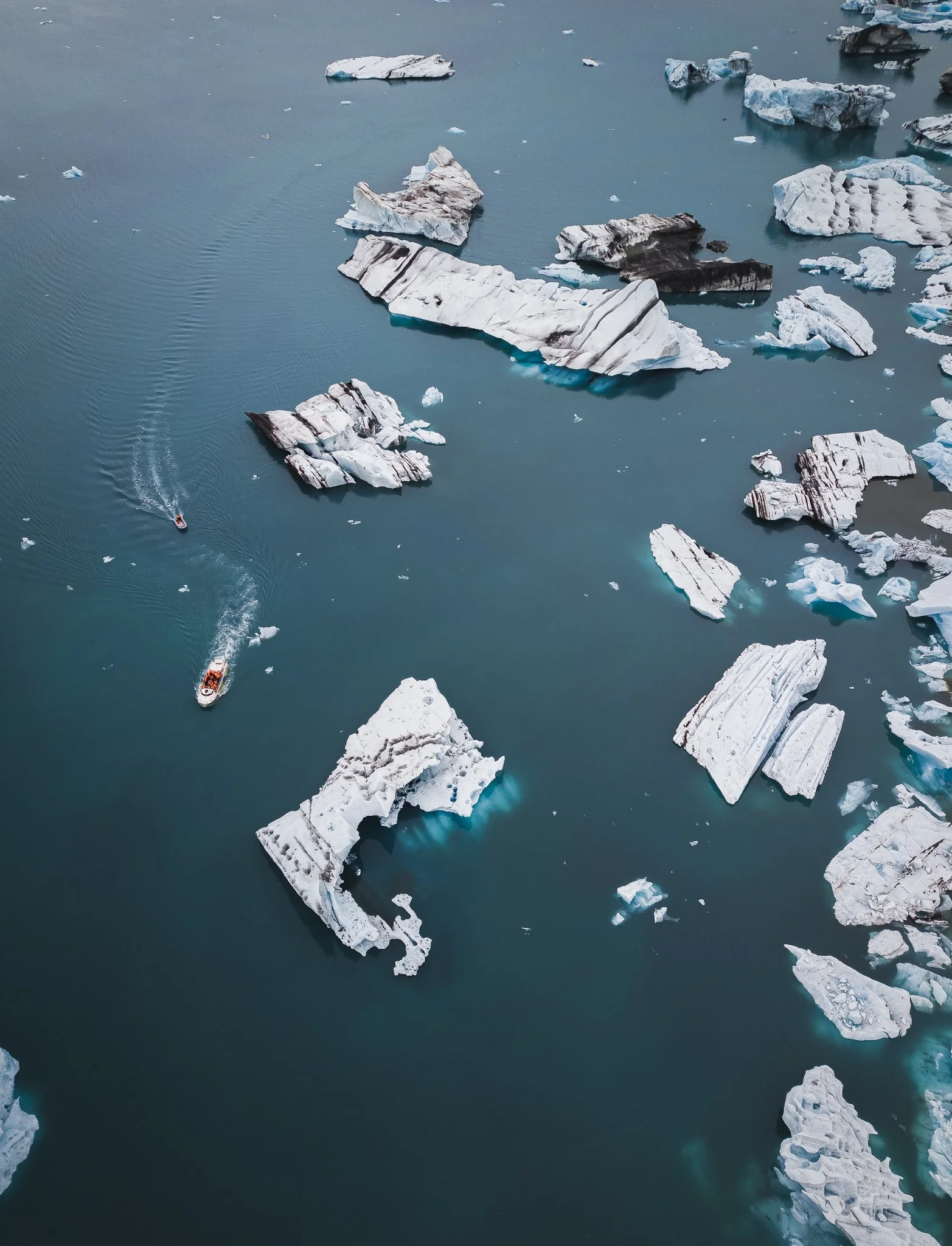 An aerial view of a body of water with scattered icebergs and a small boat creating ripples.
