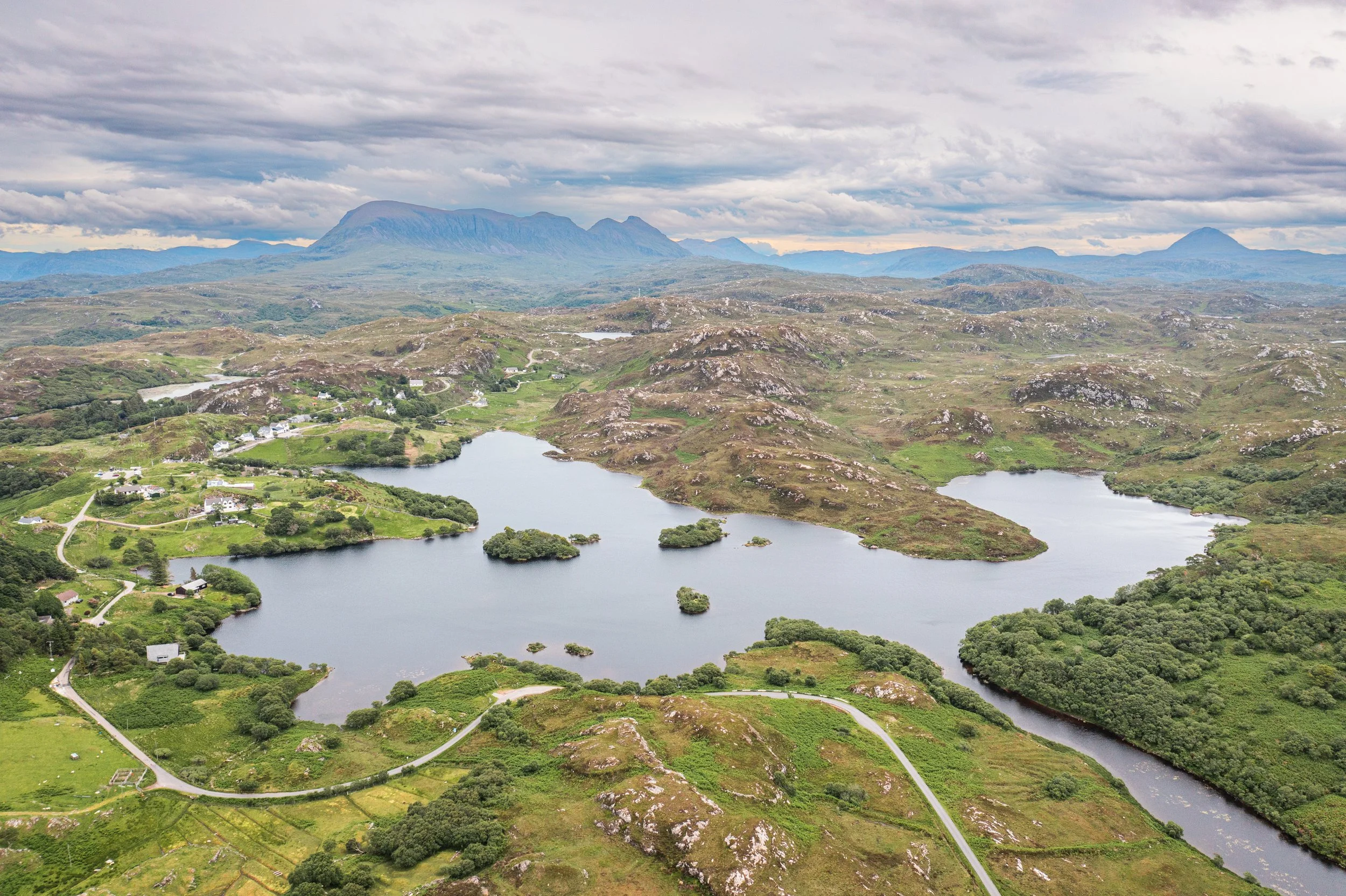 A scenic landscape with mountains in the background, lakes, and green fields with houses and winding roads.