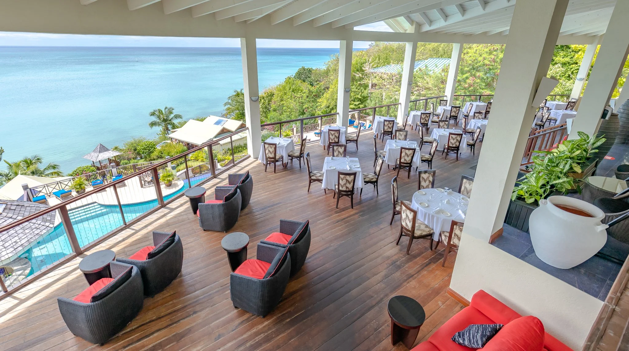 Seaside restaurant with outdoor dining area overlooking the ocean, with tables set with white tablecloths and chairs, some with view of the water, and a pool on the deck.