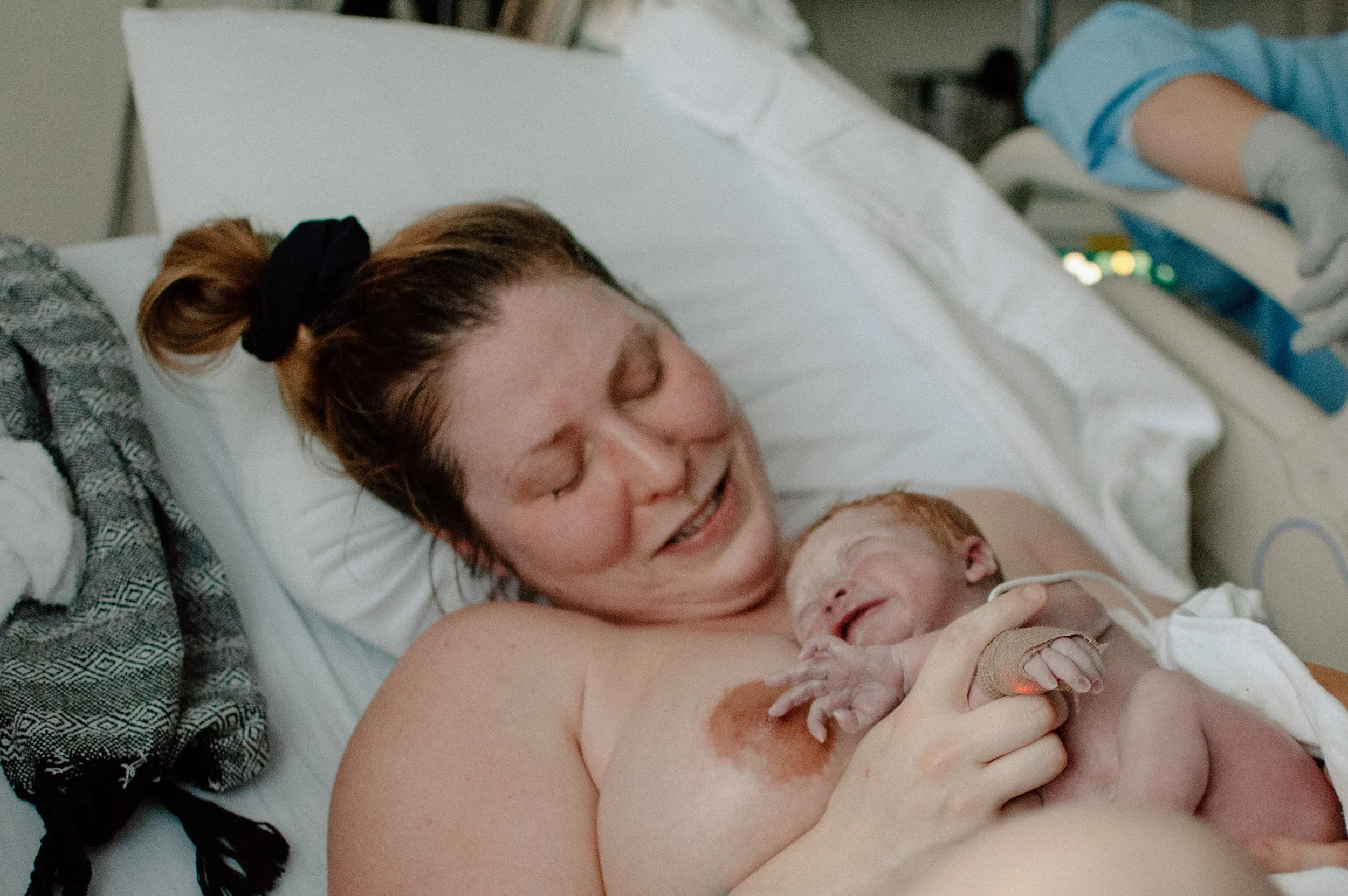 Une femme allongée dans un lit d'hôpital, tenant un nouveau-né contre elle, tous deux souriants.
