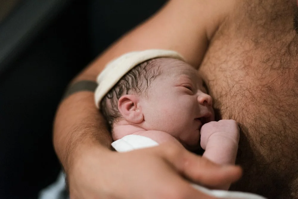 Un bébé nouveau-né en train de téter le sein d'un adulte, probablement la mère, dans un cadre chaleureux.