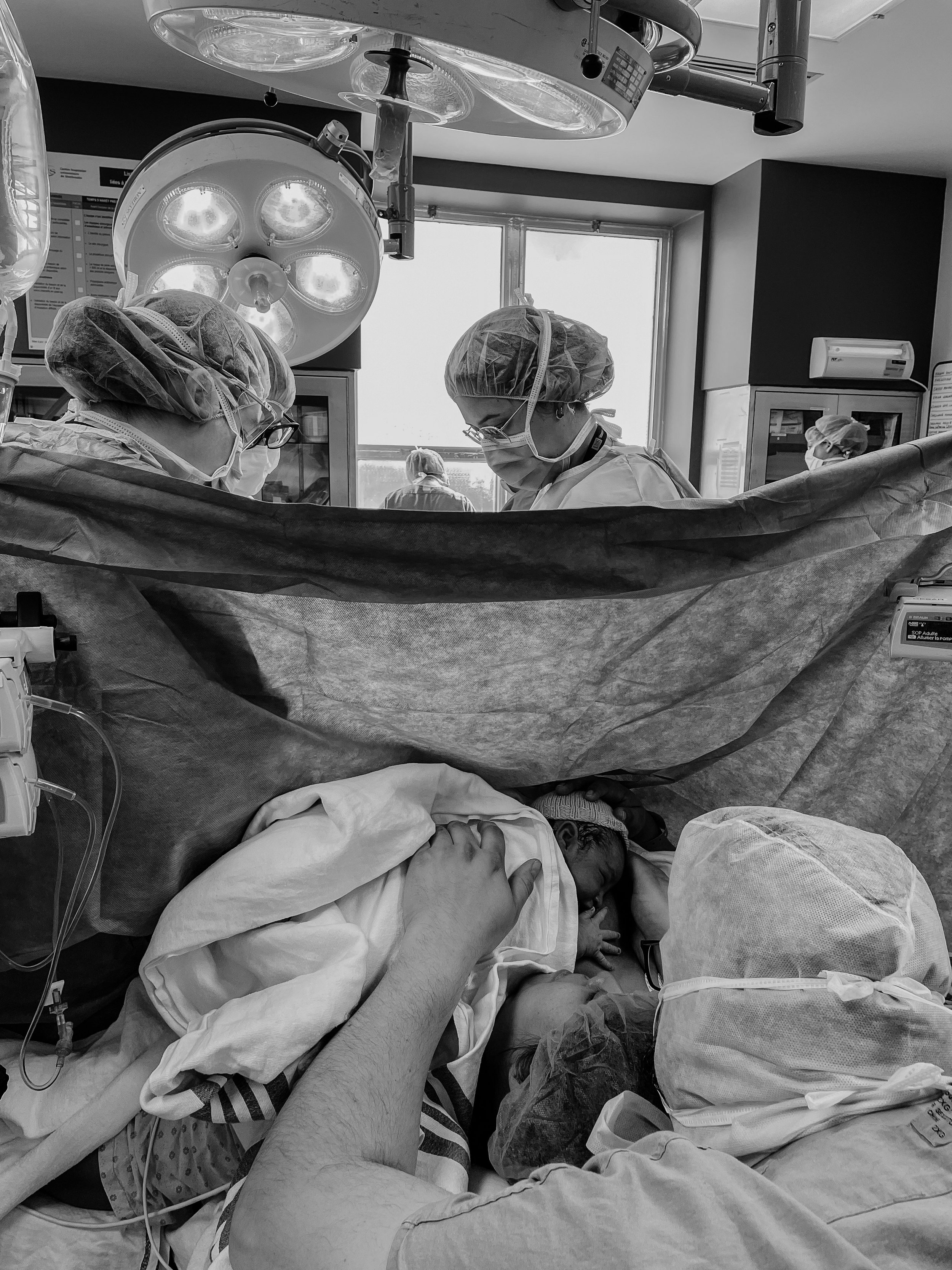 Naissance dans une salle d'opération avec médecins et infirmiers portant des blouses et des bonnets chirurgicaux. Un nouveau-né est tenu par un parent couché dans un environnement médical.