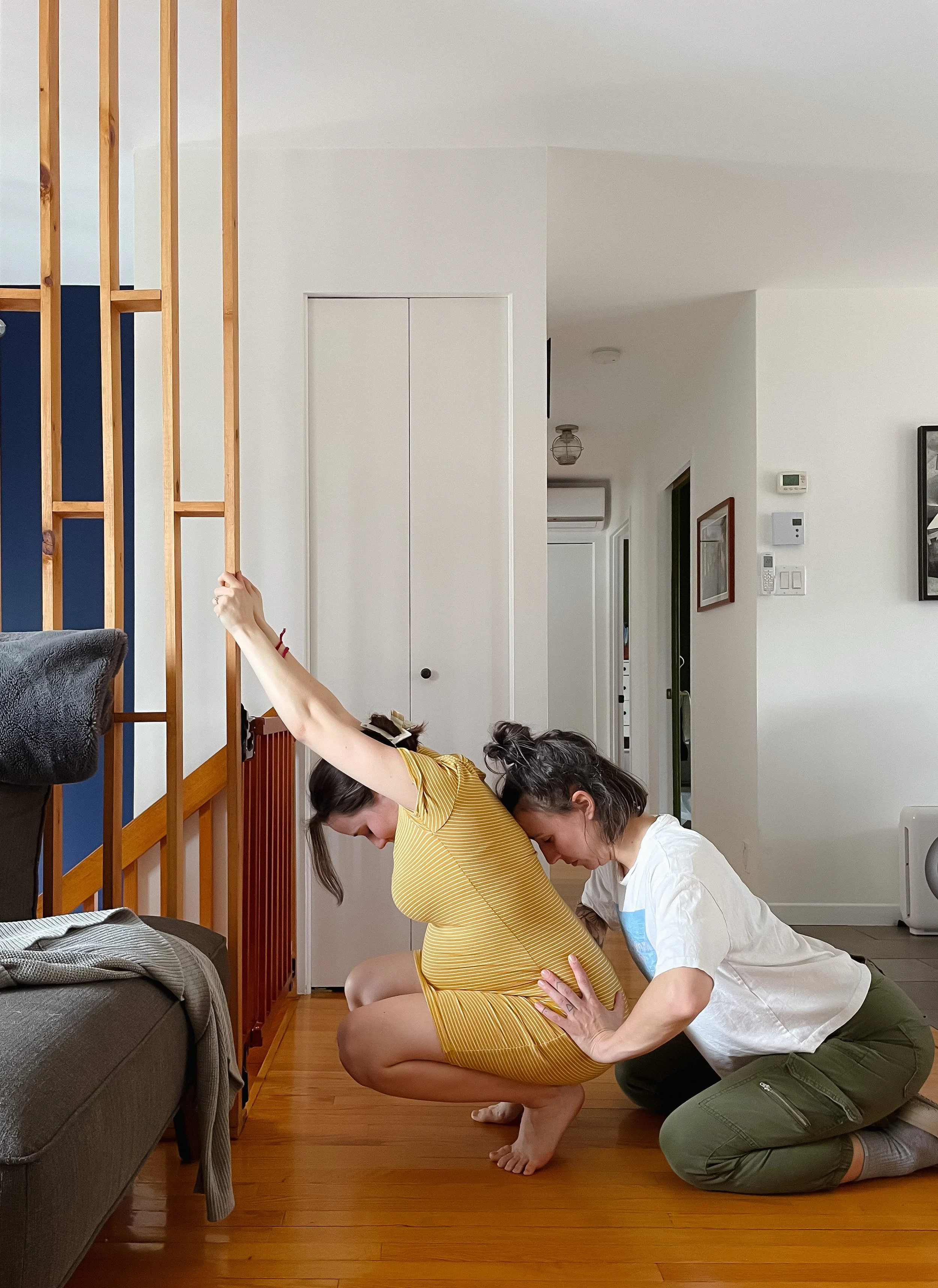 Une femme enceinte en robe jaune s'accroupit avec le soutien d'une autre personne dans une pièce. Cours prénataux au privée a Sherbrooke