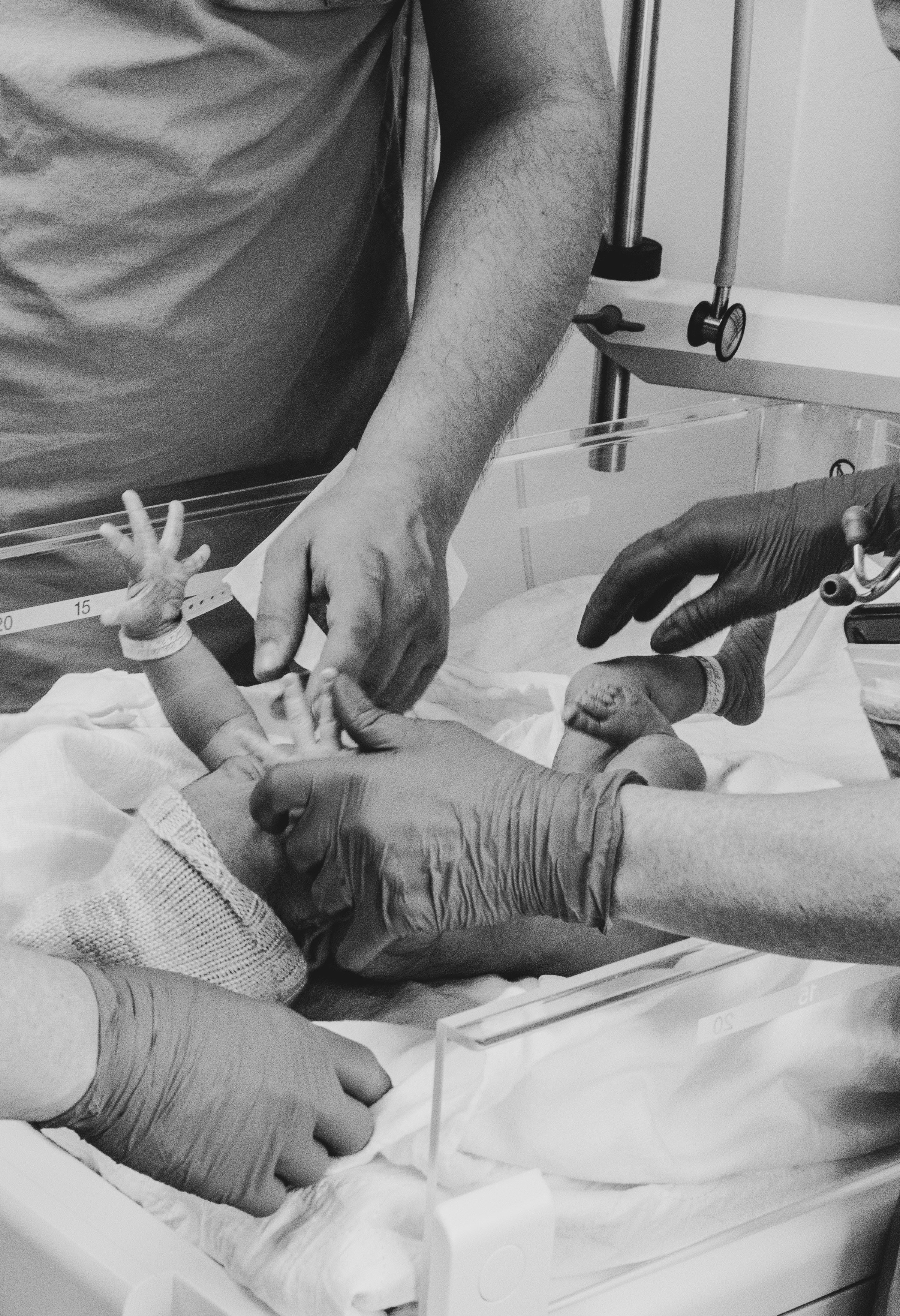 Un nouveau-né dans une couveuse entouré de plusieurs adultes qui s'occupent de lui, certains portant des gants.