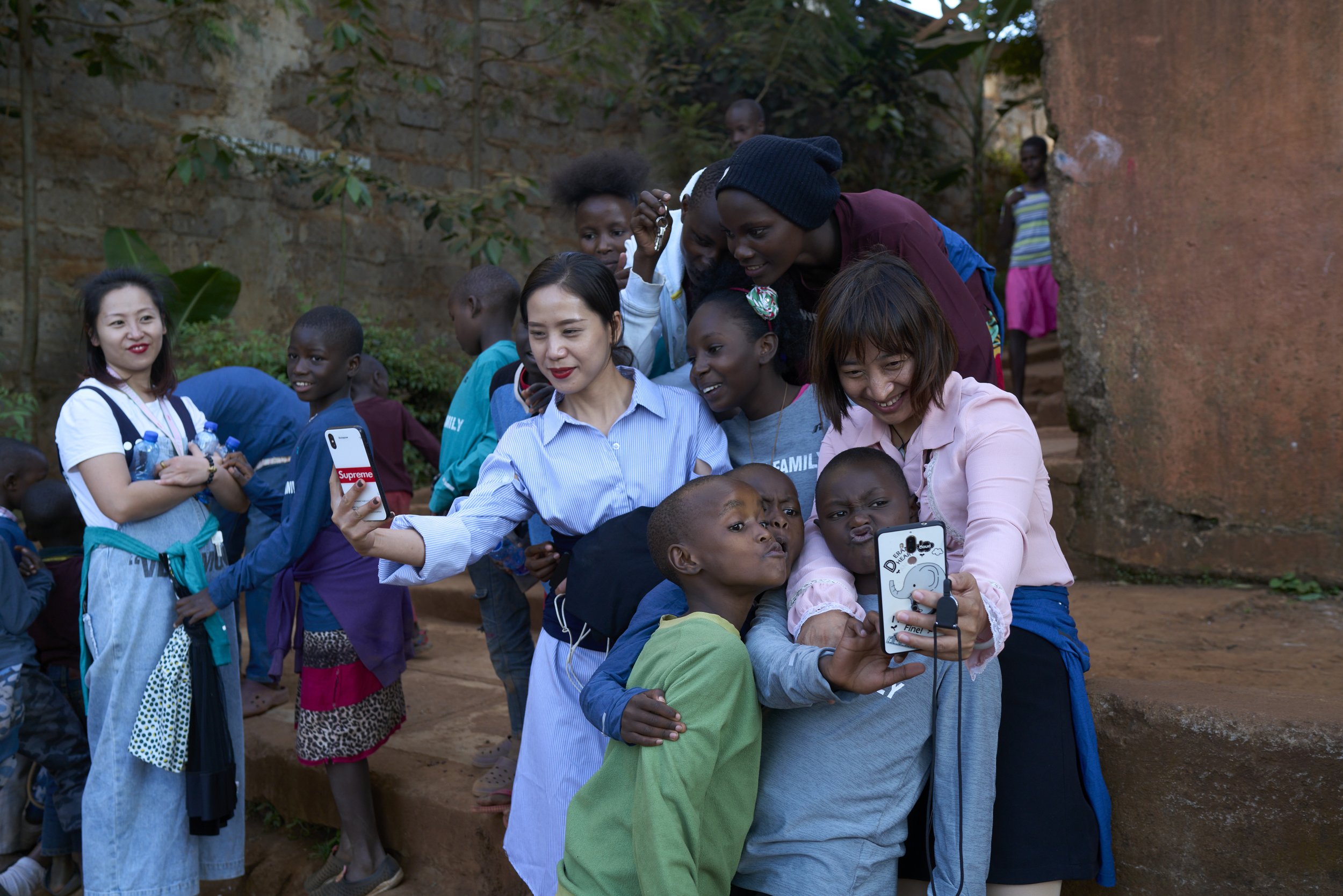 Chinese women taking selfies with Kenyan children at a charity event. Nairobi, Kenya, 2019