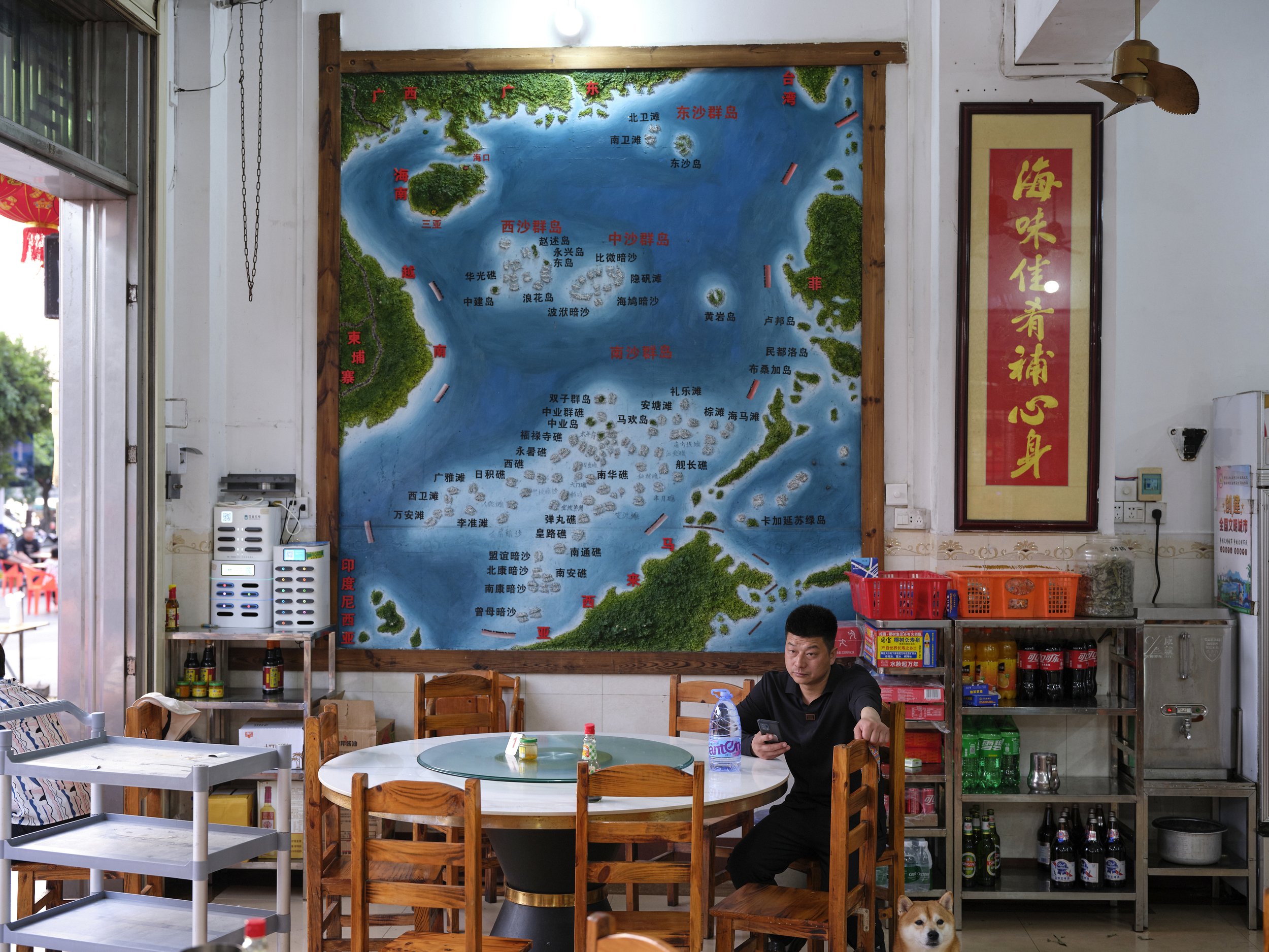 Man in restaurant in front of a map of the South China Sea and the nine-dash line. Tanmen, China, 2024