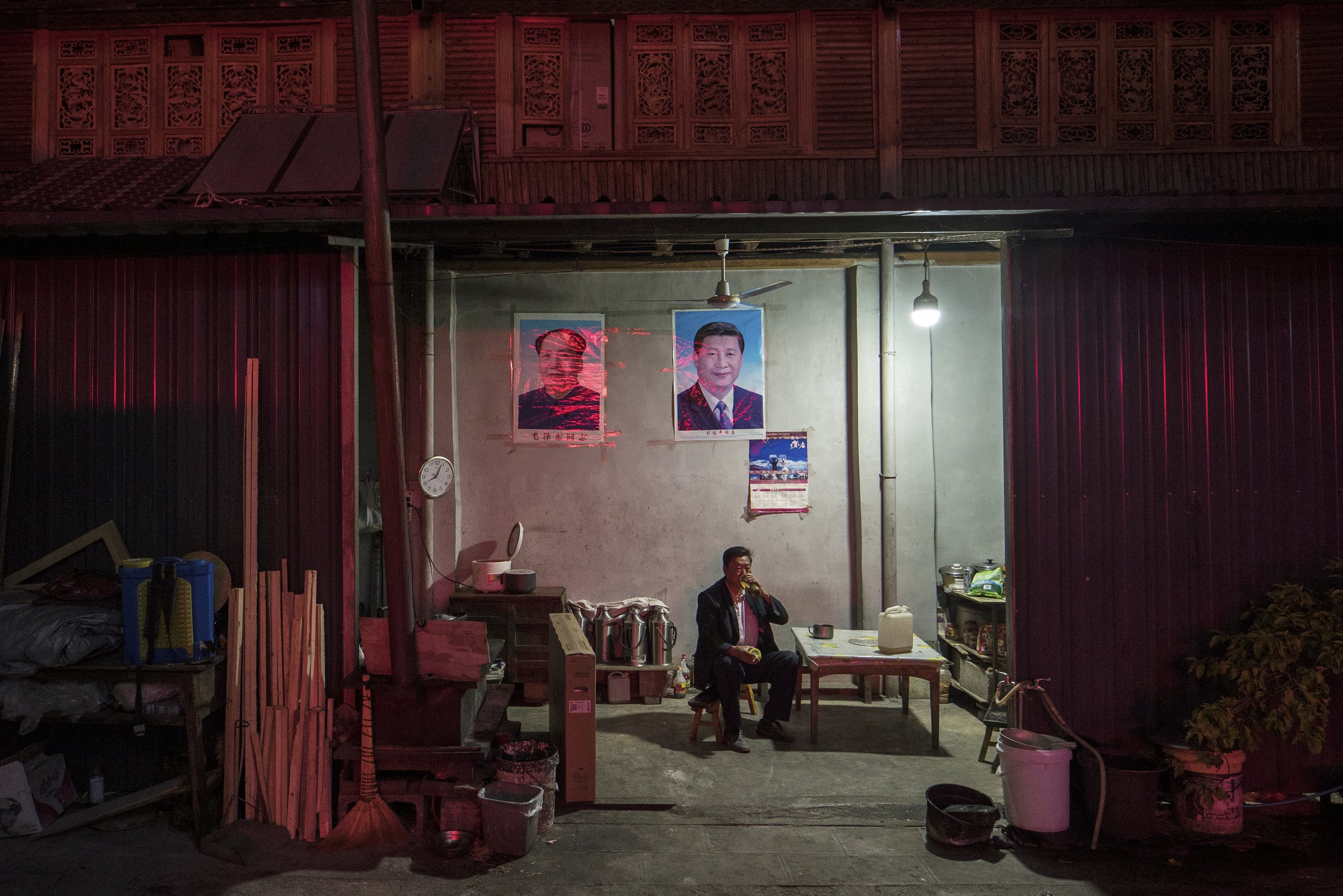 Man drinking tea under the watchful eyes of Mao Zedong and Xi Jinping. China, 2015
