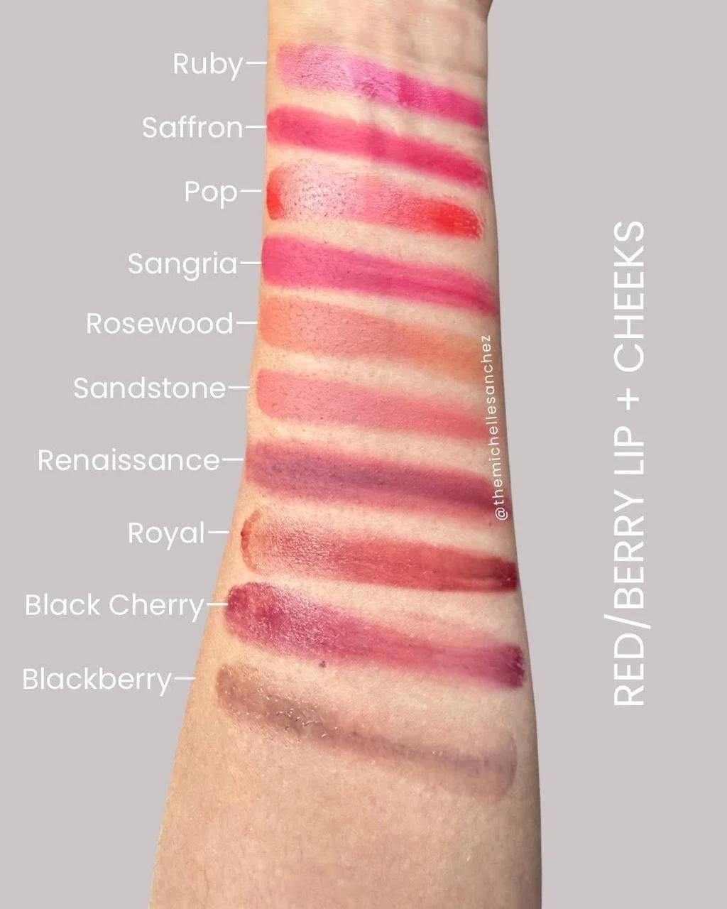 Swatch of various red, pink, and berry lipstick shades on a person's arm labeled from top to bottom: Ruby, Saffron, Pop, Sangria, Rosewood, Sandstone, Renaissance, Royal, Black Cherry, Blackberry.