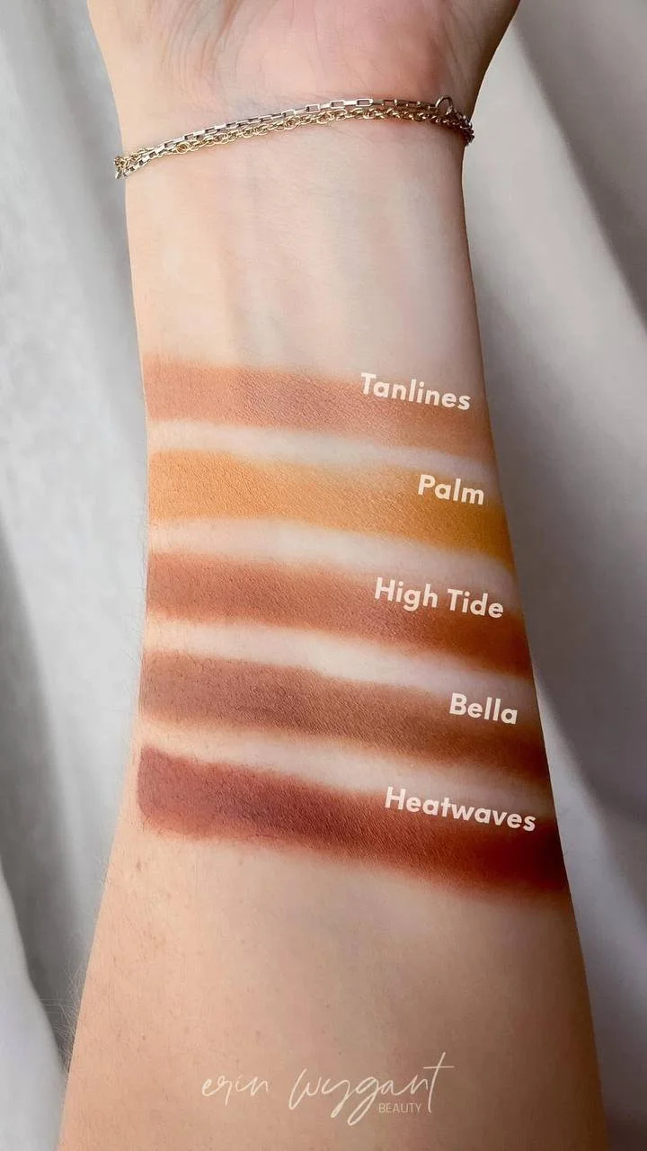 Swatch of five makeup foundation shades on a person's arm, labeled from top to bottom: Tanlines, Palm, High Tide, Bella, Heatwaves. The arm has a silver bracelet and a light skin tone.