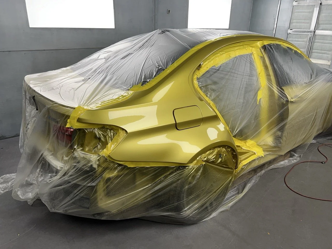Yellow sports car covered with plastic in a garage or paint booth.