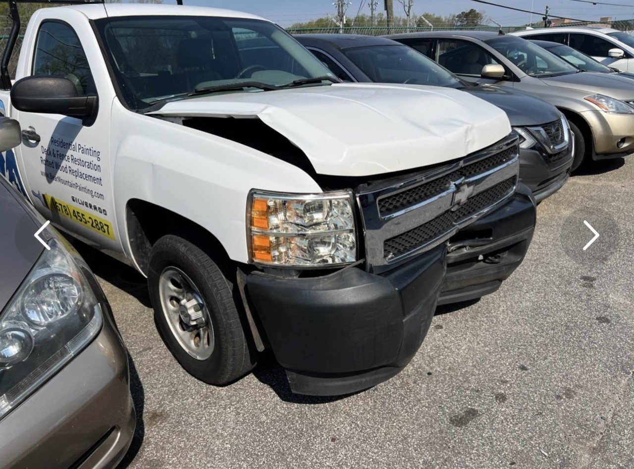 A white Chevrolet truck with front-end damage, parked in a lot with other cars.