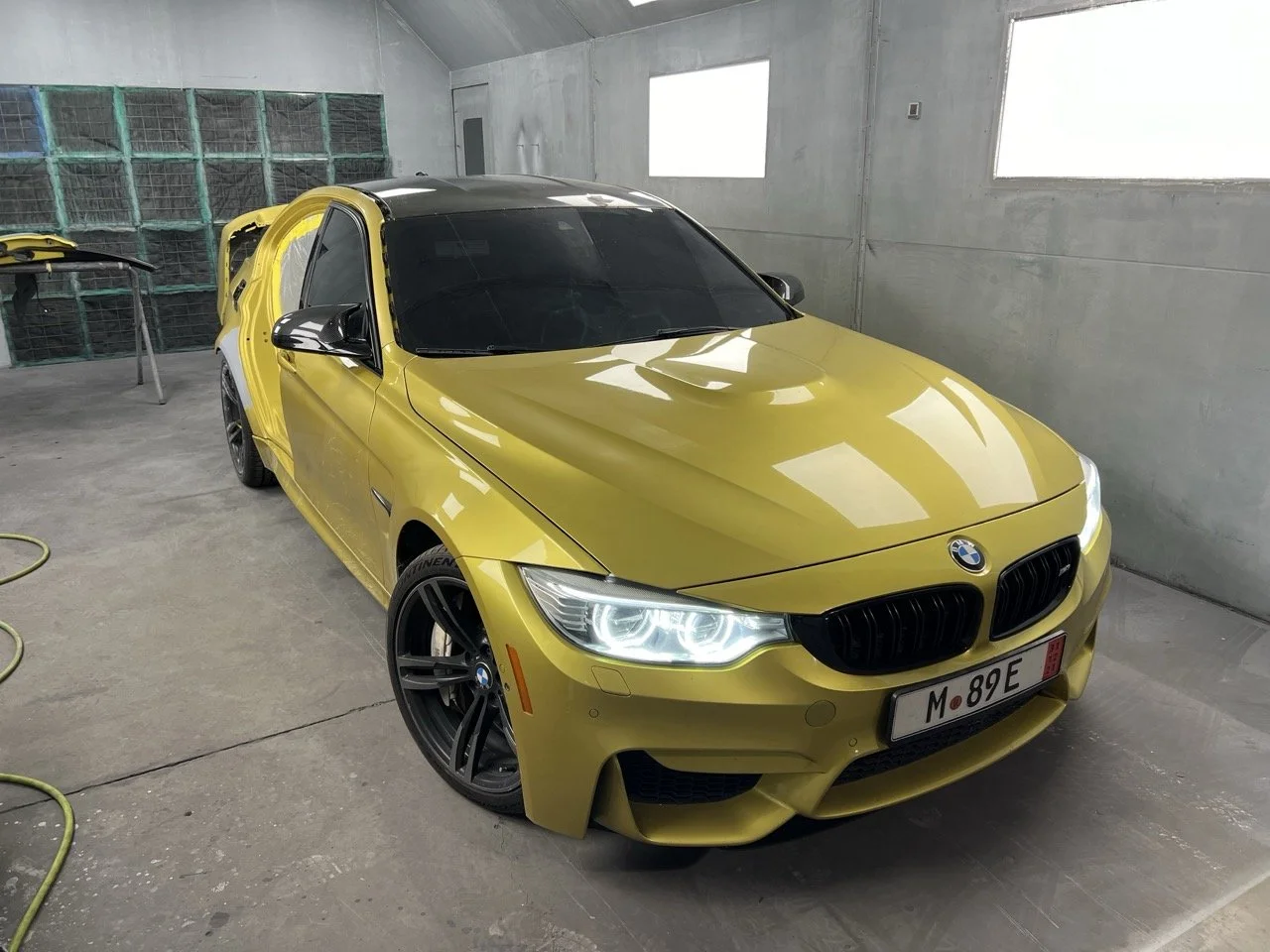 A yellow BMW sports car with black accents in an indoor garage, partially disassembled with the rear door open.