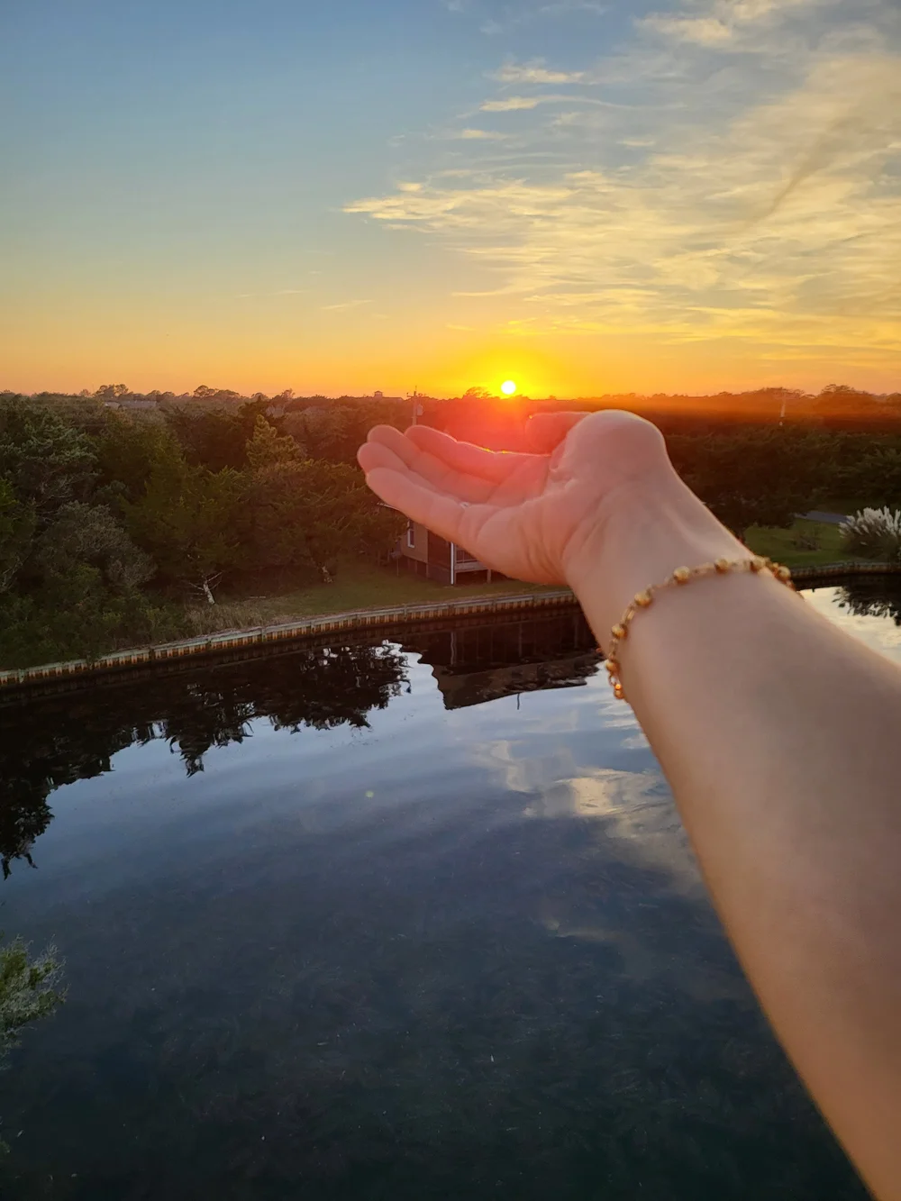 A hand held to the setting sun over the water