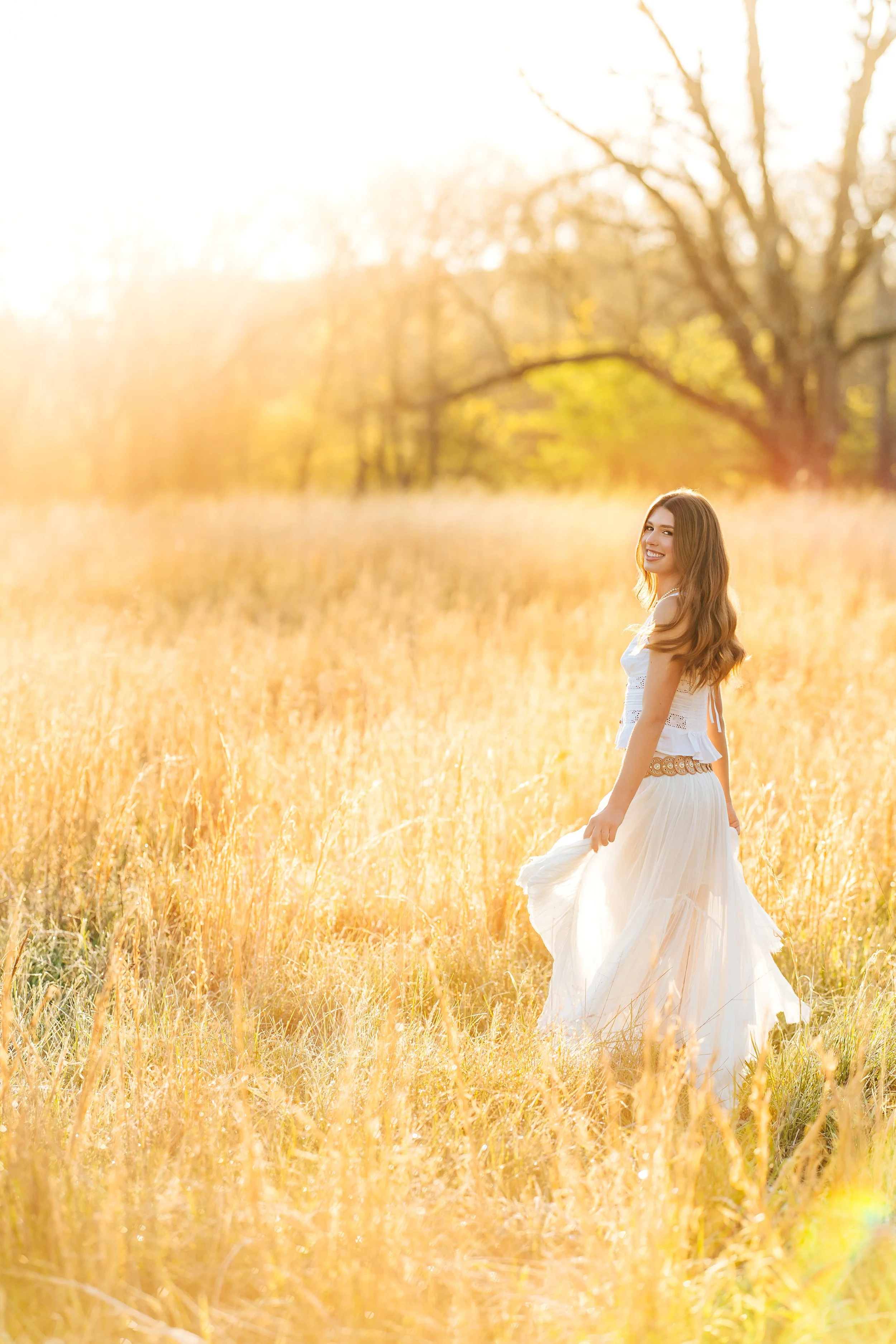 Senior twirling in a golden field wearing a white outfit, bathed in warm golden-hour tones, captured by a trusted NWA Senior Photographer.
