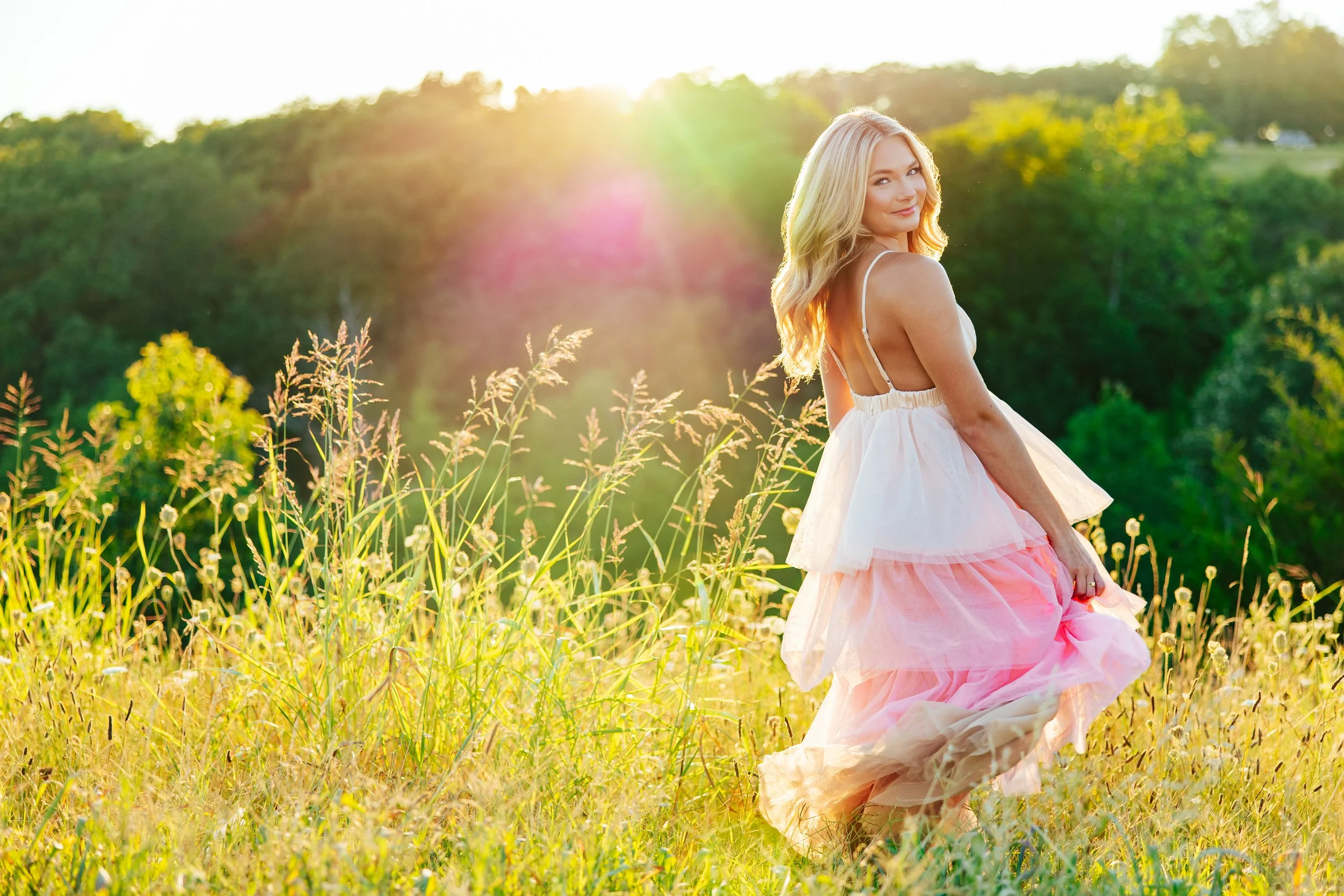 Rogers High School senior in a pink tulle dress twirling joyfully in a vibrant green field at golden hour in Fayetteville Arkansas