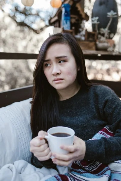 Woman sitting with mug of coffee looking to side with slight frown