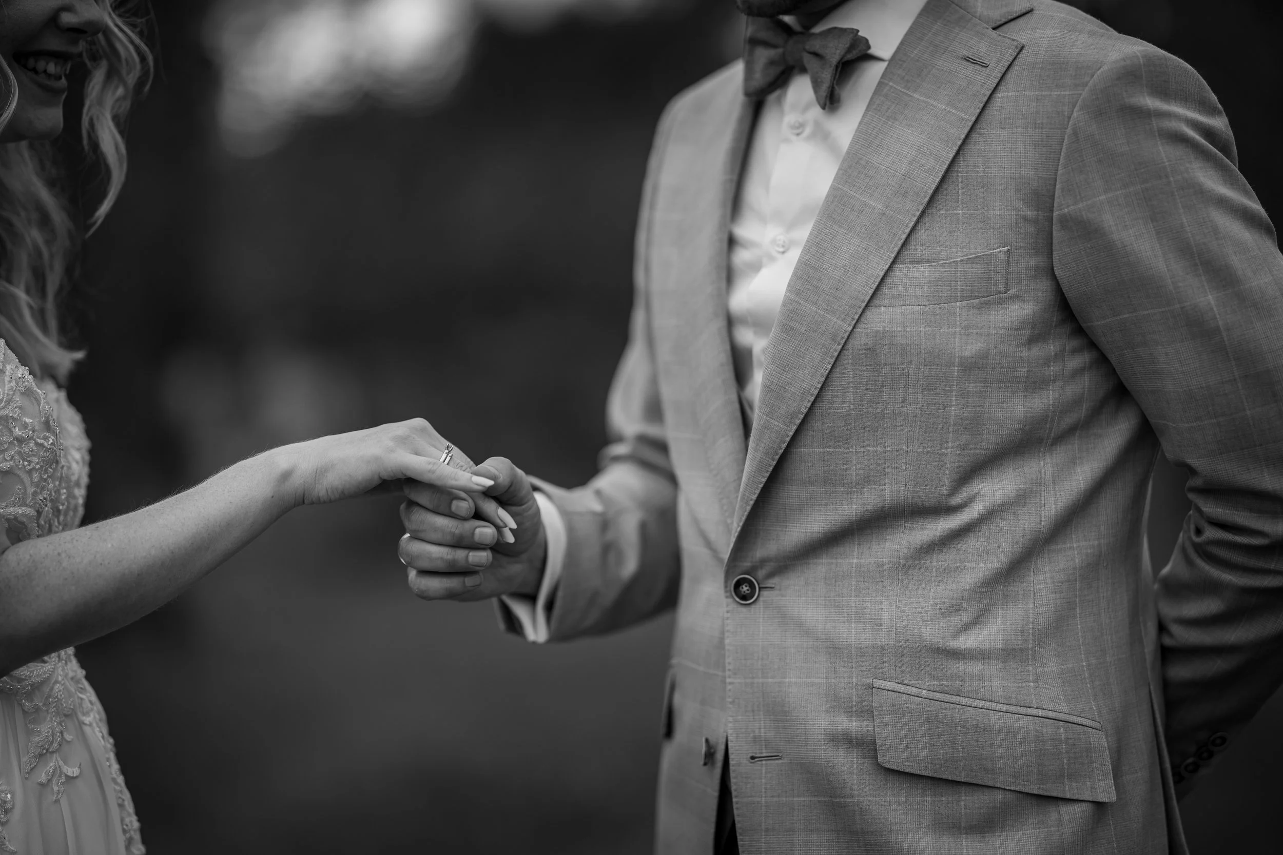 Ein Brautpaar bei der Trauung, das sich die Hand hält, in Schwarz-Weiß aufgenommen.