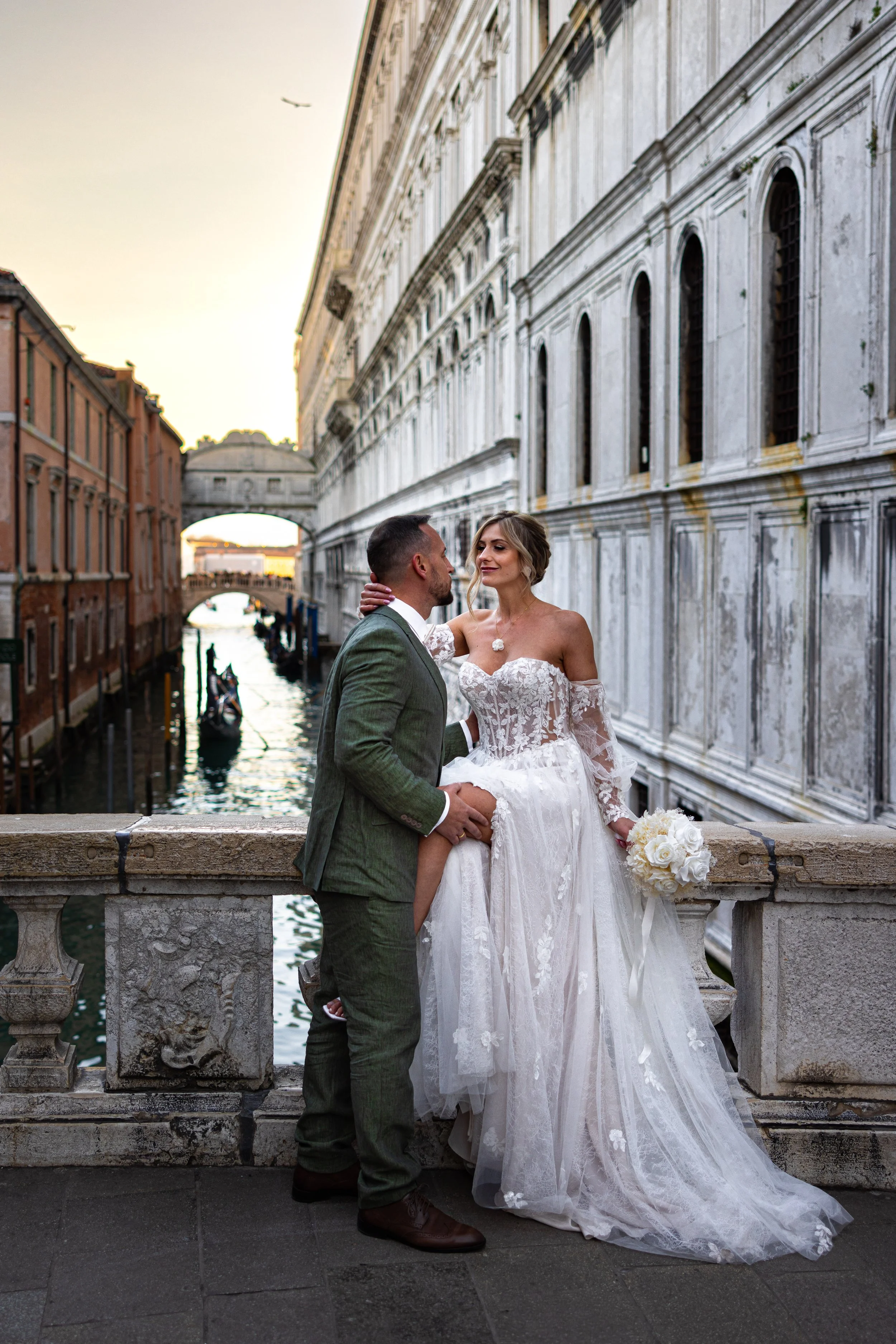 Ein Hochzeitsfoto von einem Paar in einem Kanal in Venedig bei Sonnenuntergang, mit einer Brücke im Hintergrund.