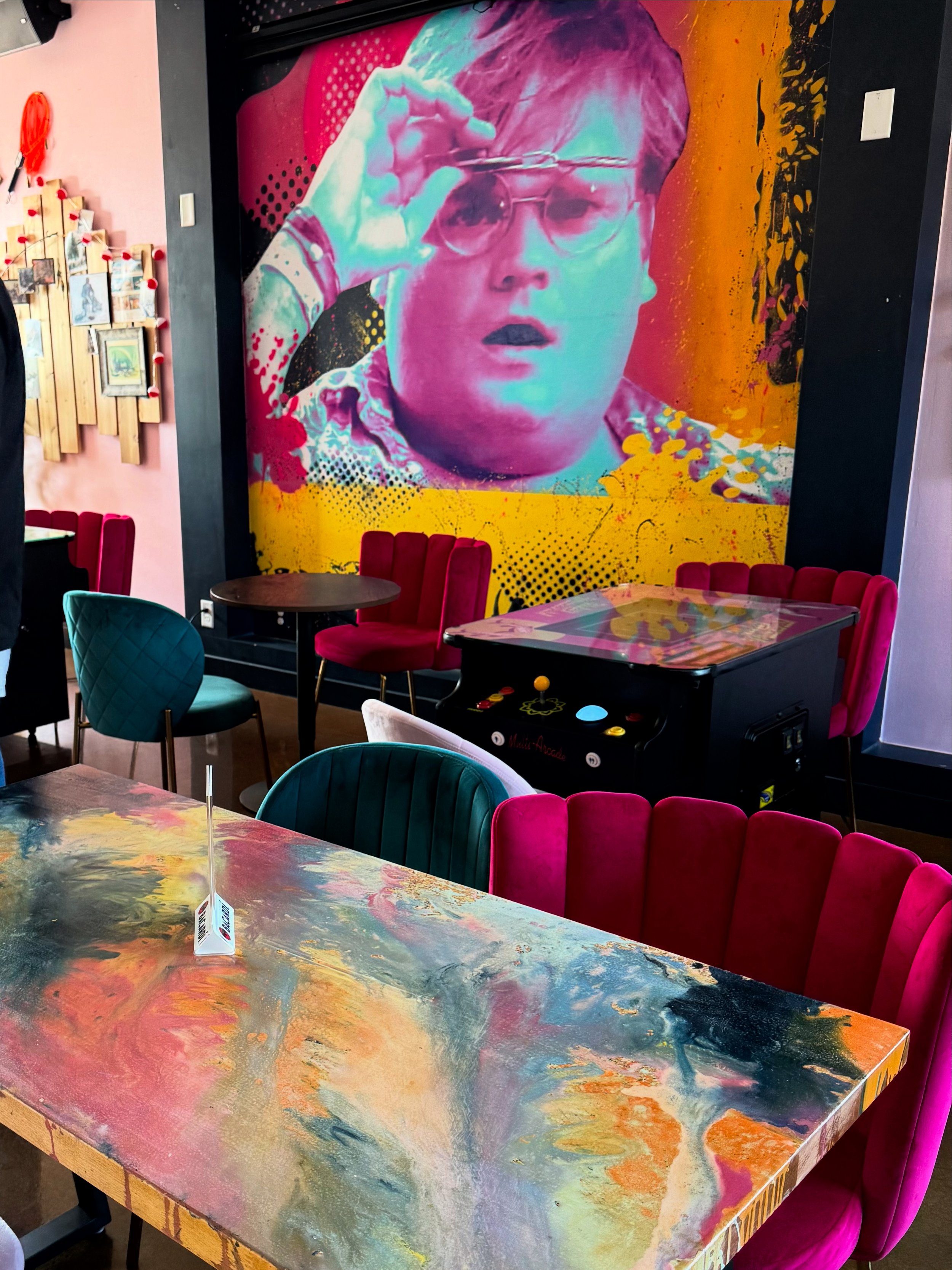 Colorful mural of a person wearing glasses, with a surprised expression, painted on a wall in a vibrant, modern restaurant or café.