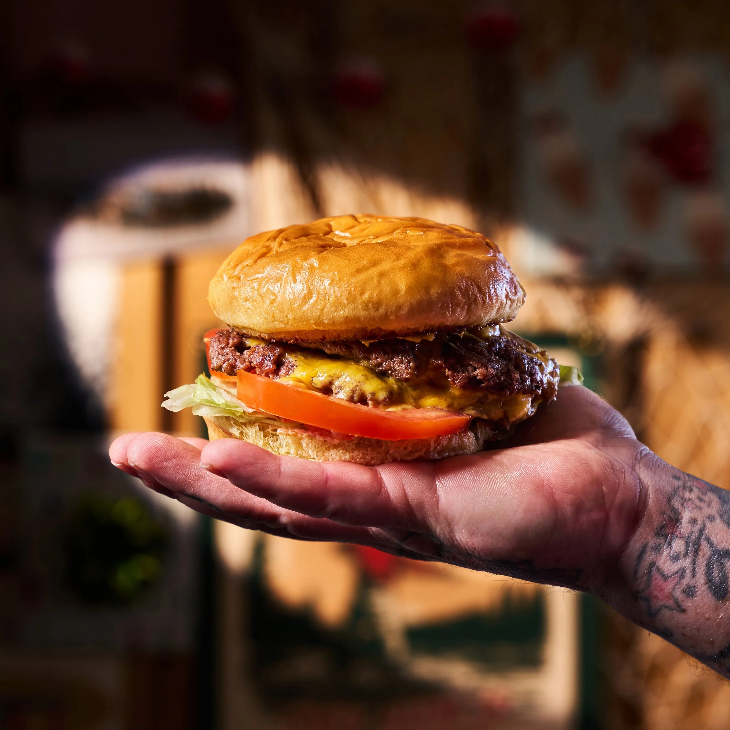 Hand holding a cheeseburger with lettuce, tomato, beef patty, and melted cheese on a toasted bun.