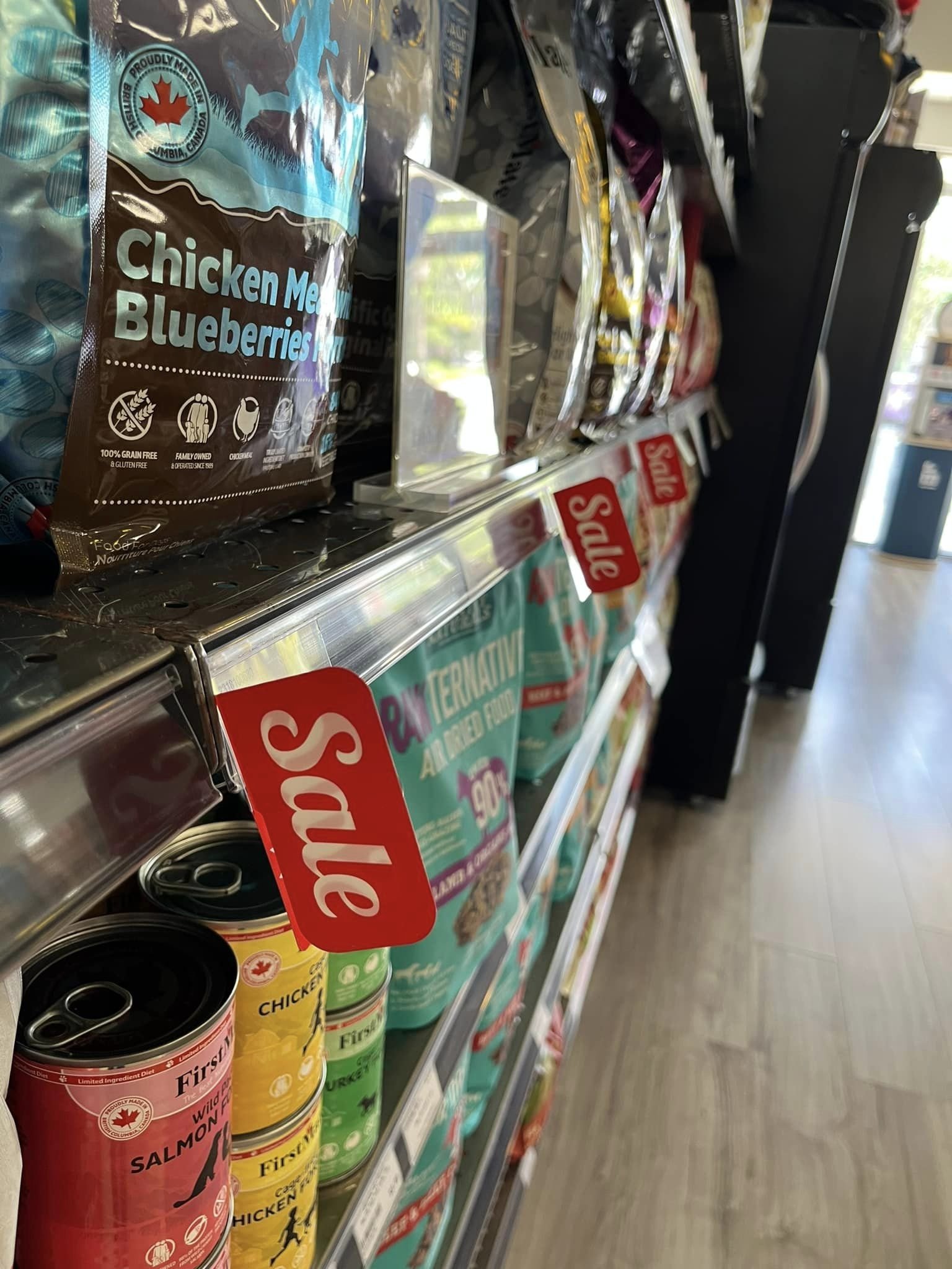 Shelves in a grocery store with pet food and canned cat food, including bags labeled chicken and blueberries for pets, and cans of salmon, chicken, and turkey cat food.