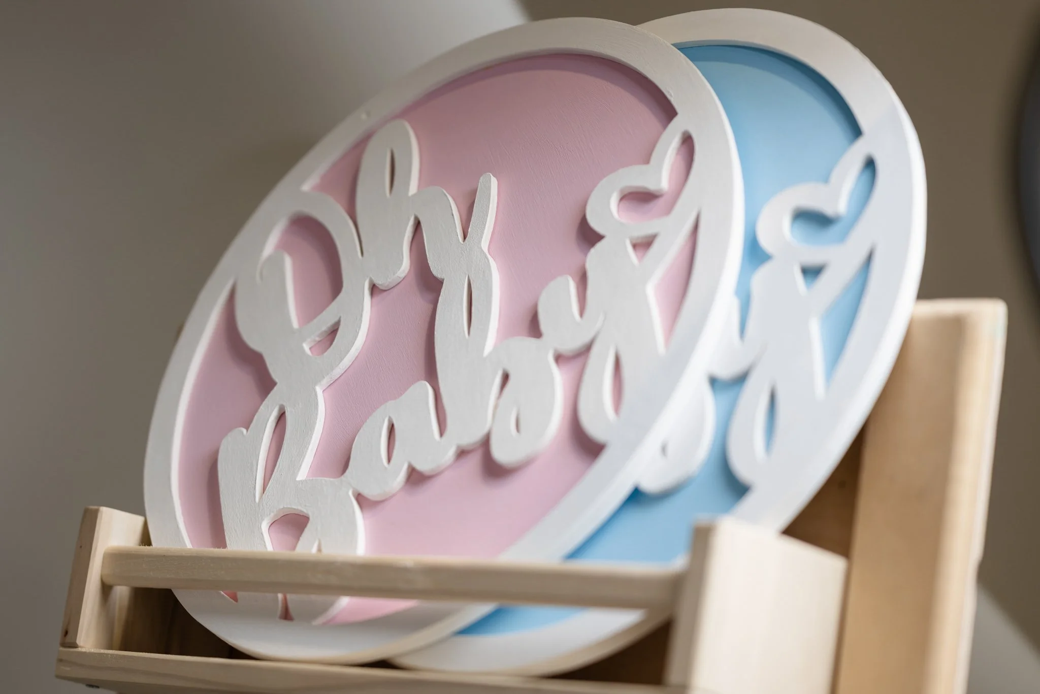 Decorative sign with the phrase 'baby family' in white cursive letters, pink and blue background, on a wooden stand.