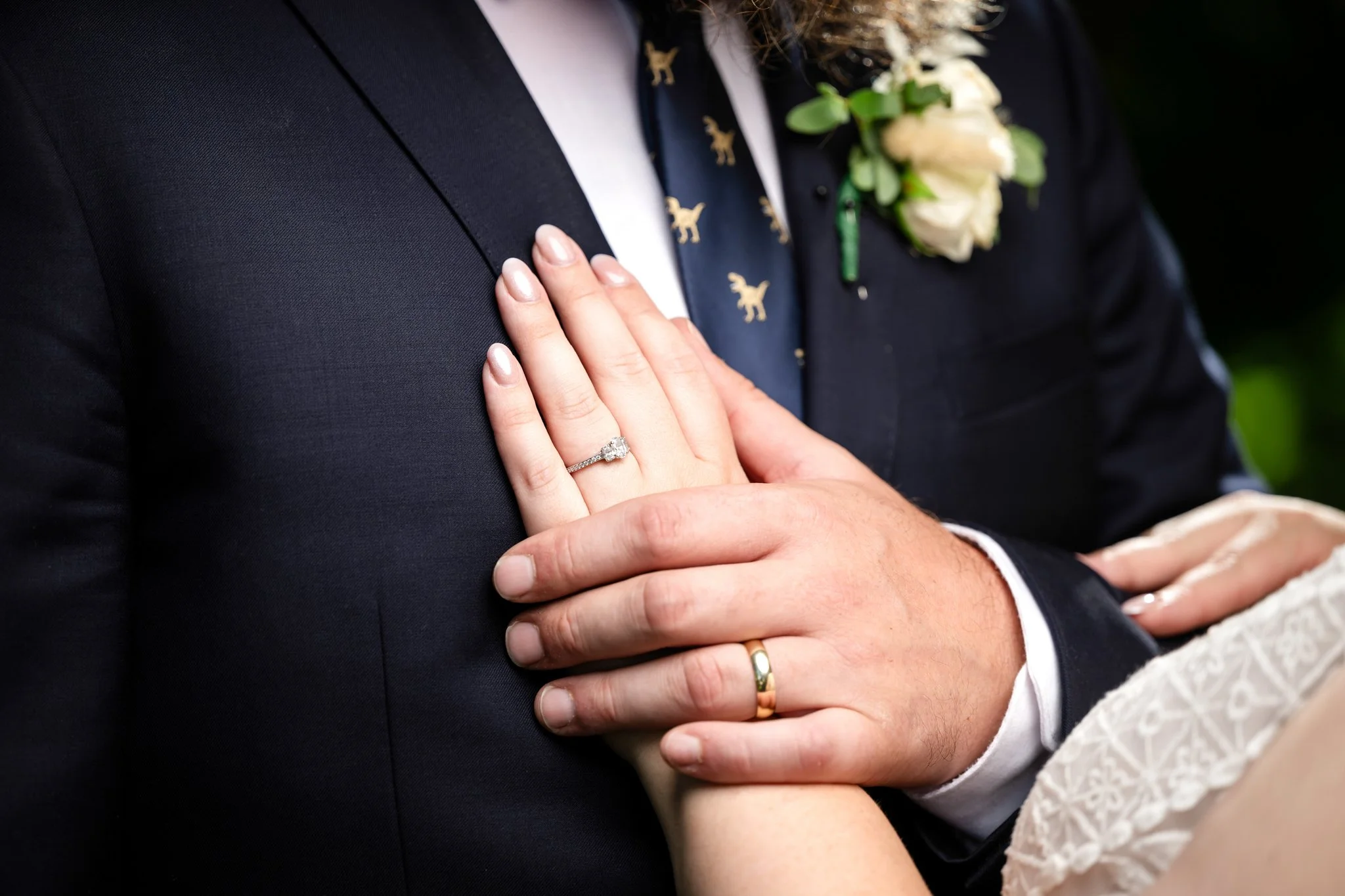 Close-up of a bride and groom's hands showing wedding rings, with the bride wearing a diamond ring on her finger, during a wedding ceremony.