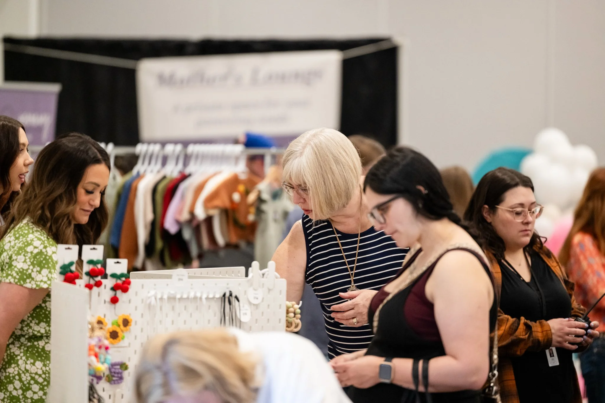 Women browsing through craft or jewelry display at an indoor market or fair.