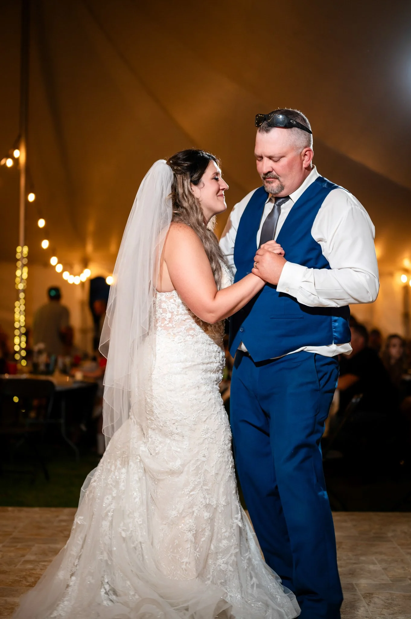 Bride and groom sharing a dance at their wedding reception, holding hands and gazing at each other under warm lighting.