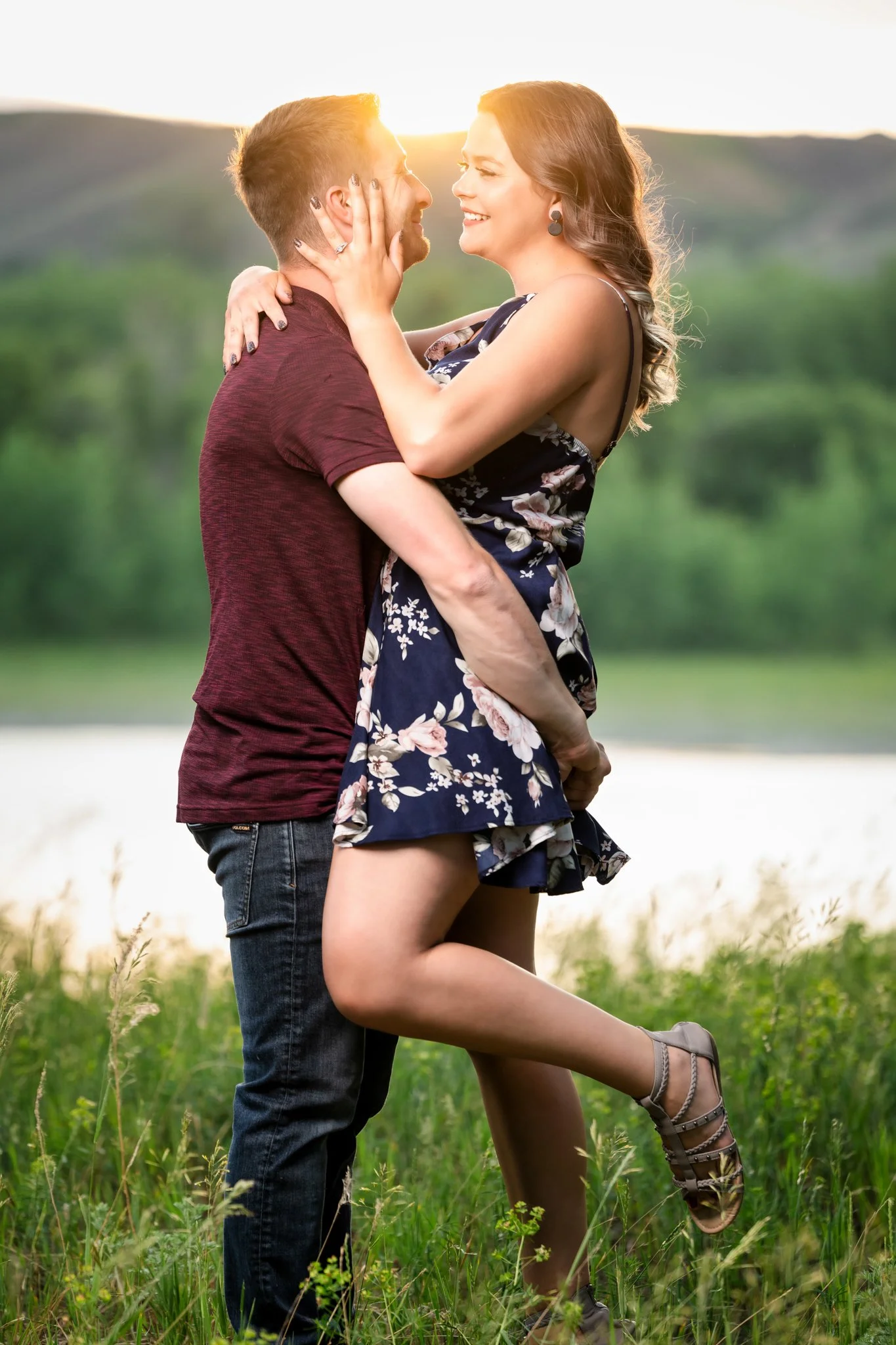 A couple embracing outdoors during sunset, with the woman lifting her leg and smiling.