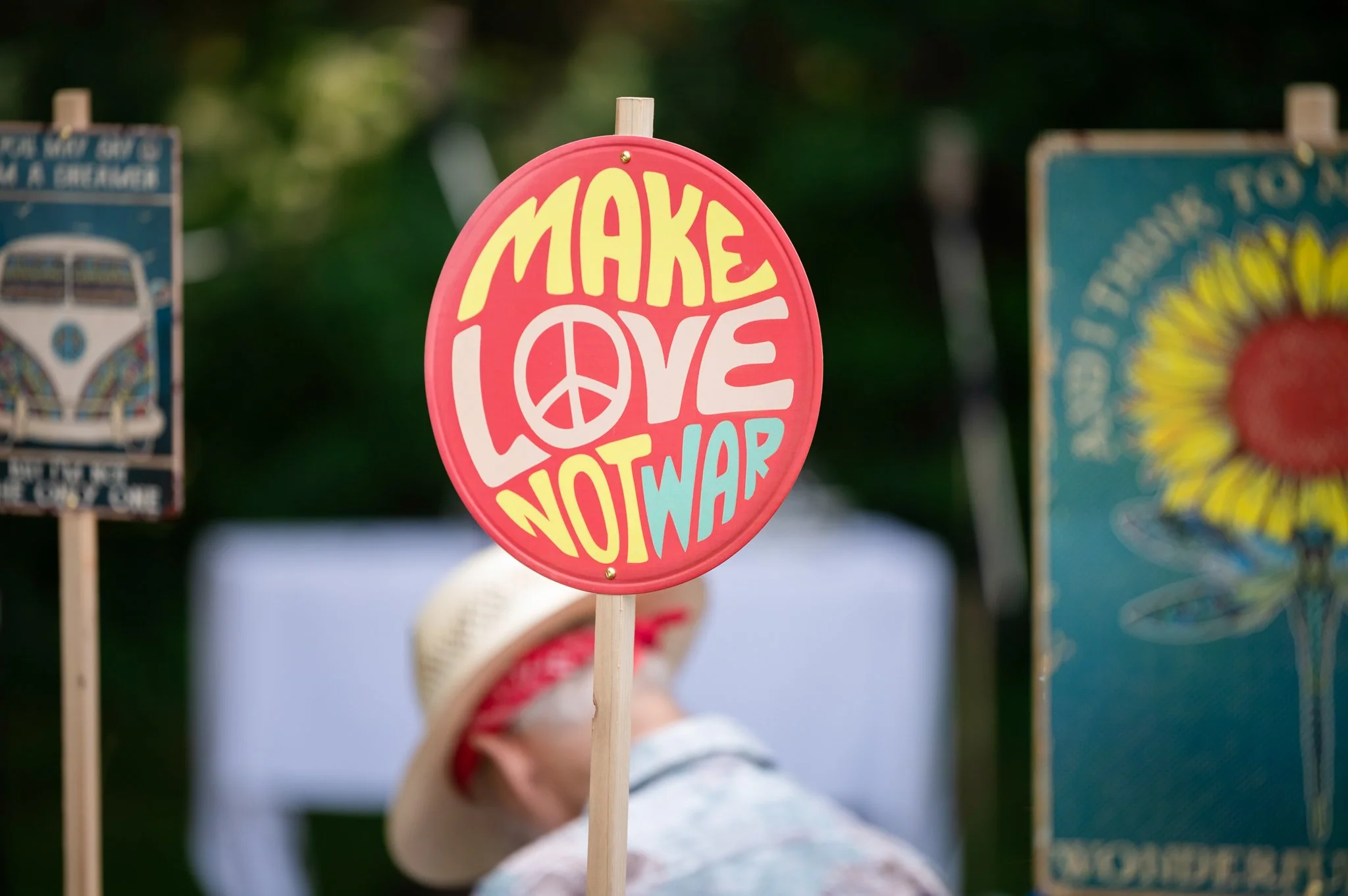 Pink sign with yellow, white, and blue text reading 'MAKE LOVE NOT WAR' and a peace symbol in the word 'LOVE'.