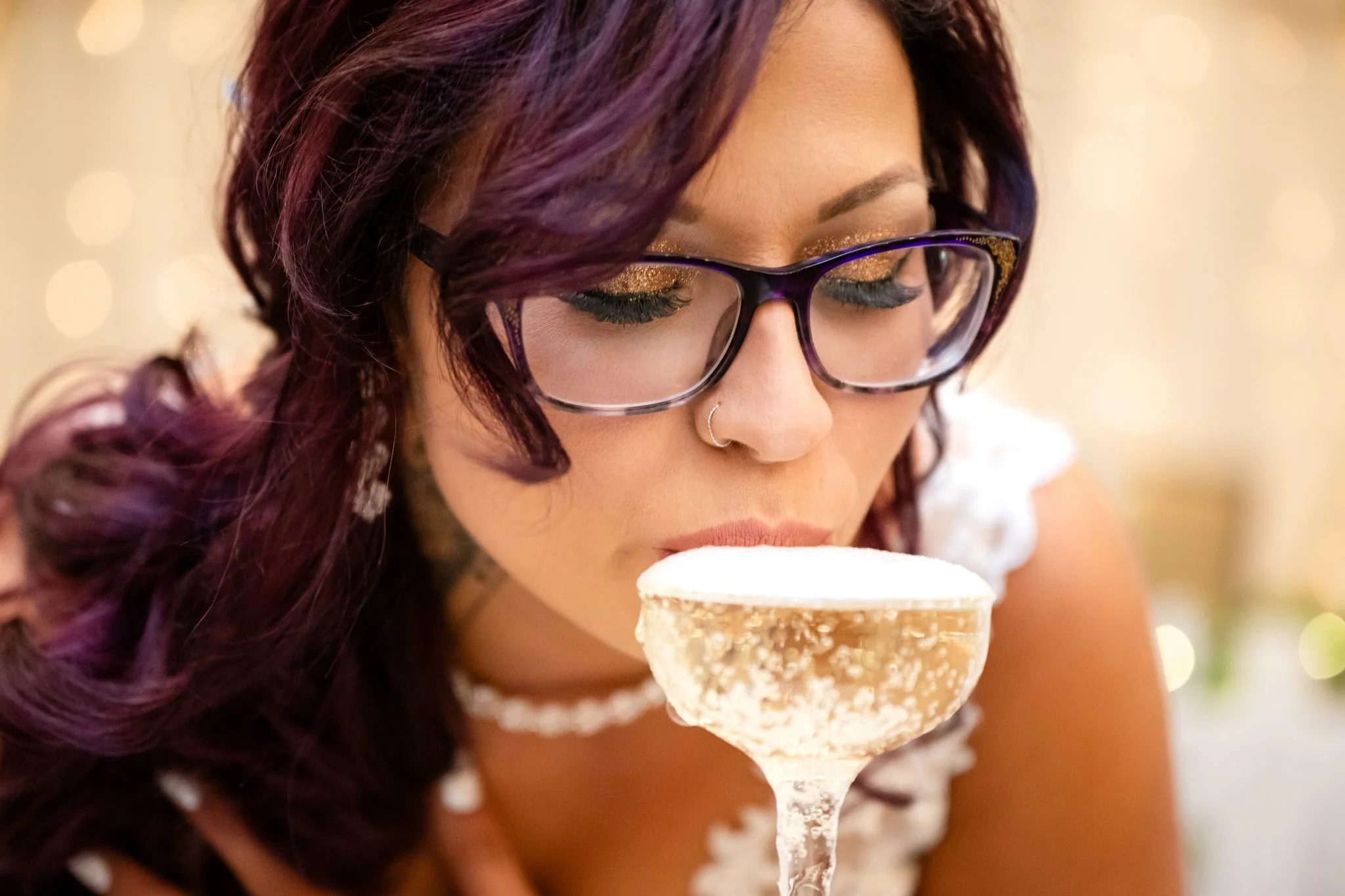 Woman with purple hair and glasses smelling a cocktail in a coupe glass.