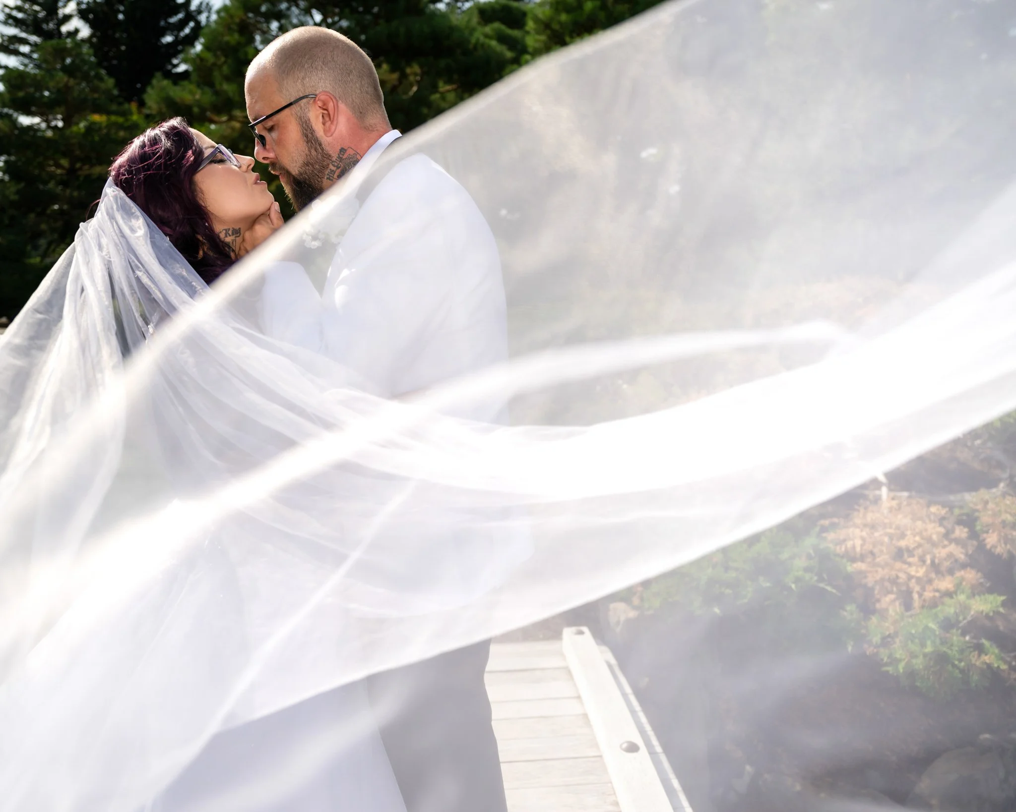 A bride and groom sharing a kiss outdoors, with the bride's veil flowing around them.