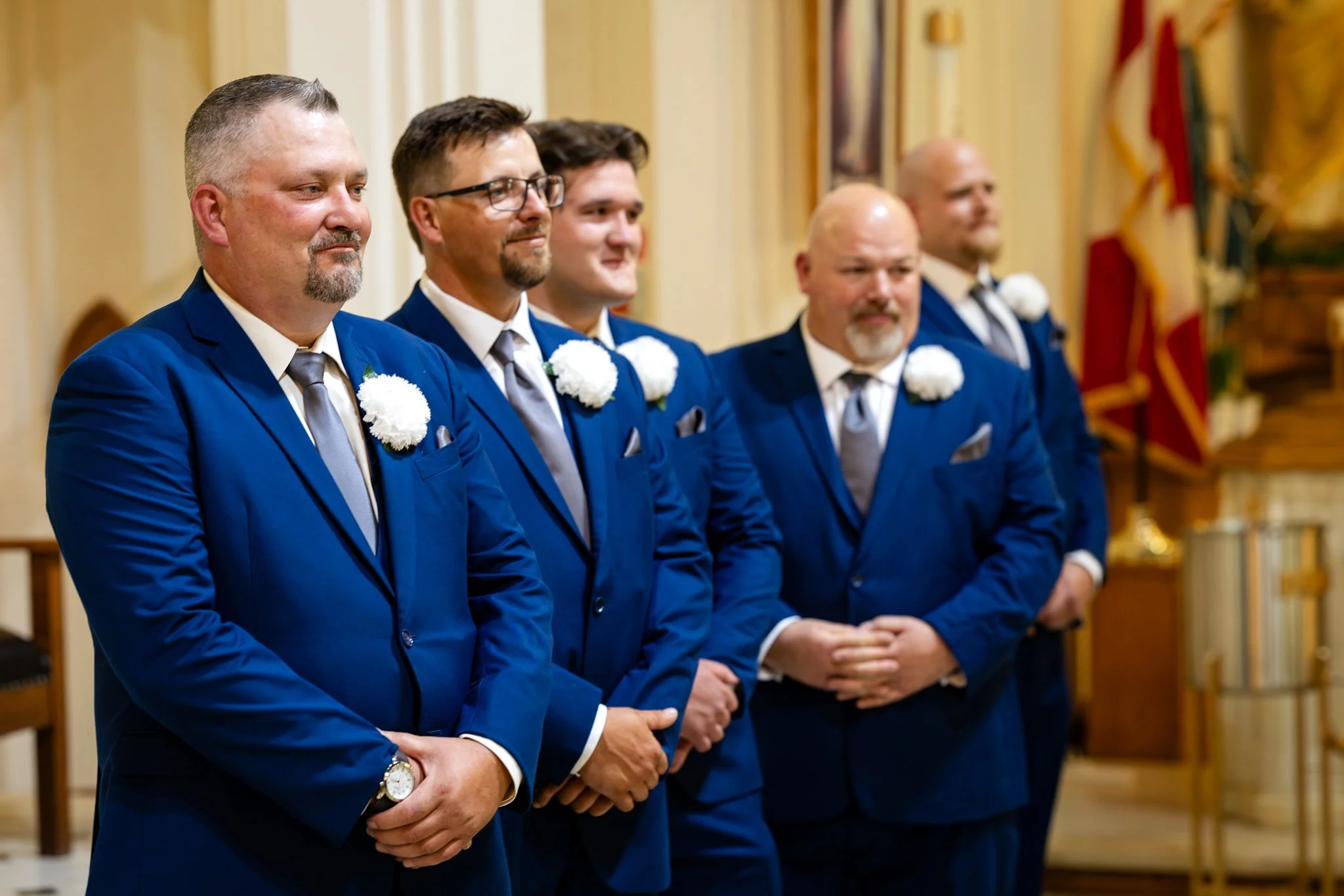 Groomsmen in blue suits with white flowers at a wedding ceremony.