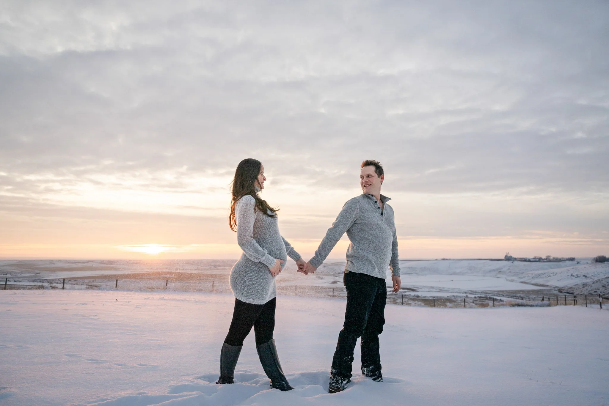A couple holding hands in a snowy field during a sunset.