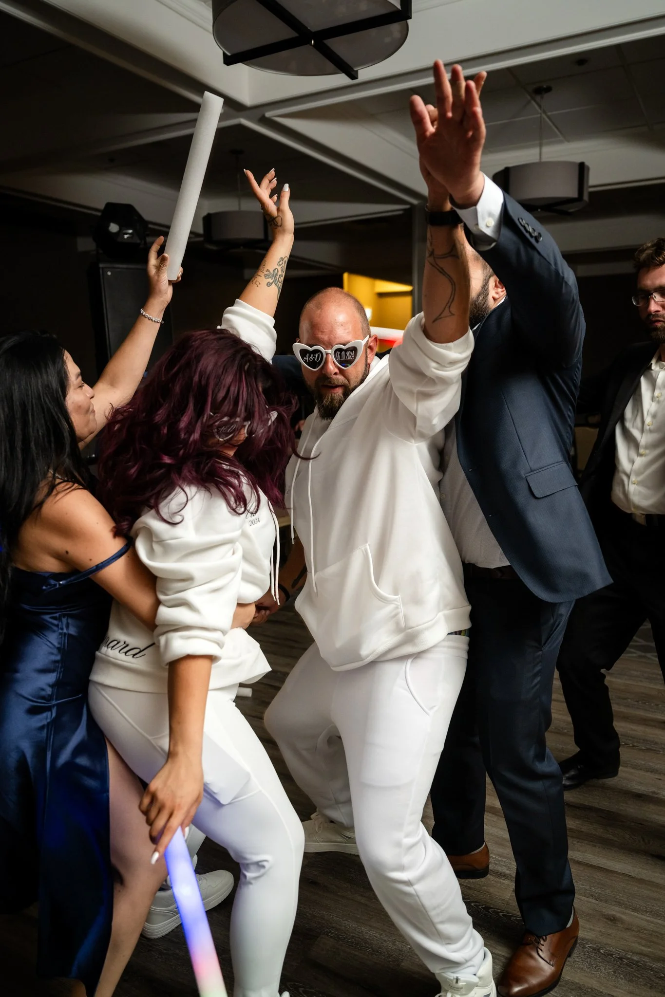People dancing and celebrating at a party, some wearing fun accessories, in a decorated indoor venue.
