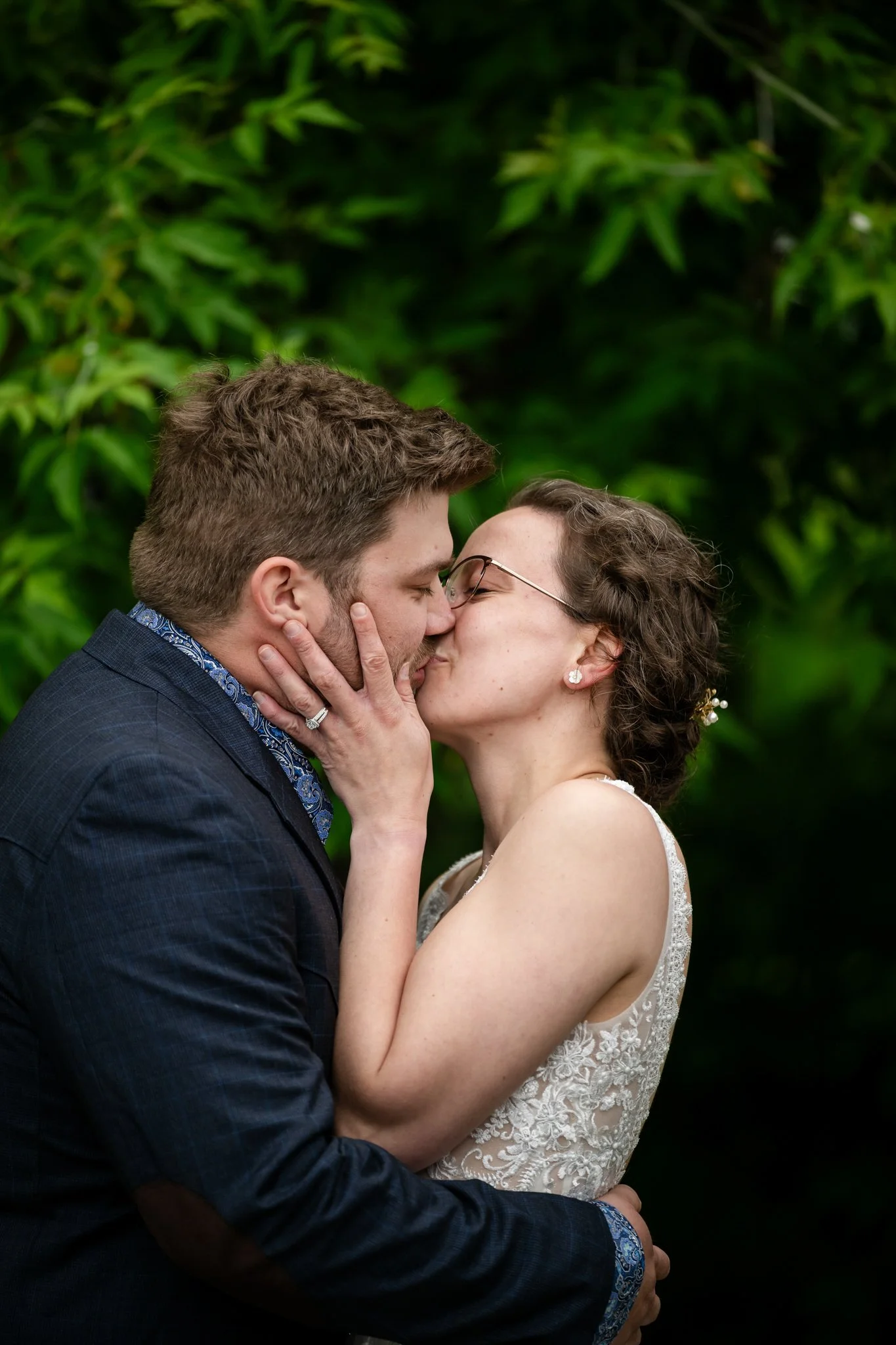A couple sharing a kiss outdoors with greenery in the background.