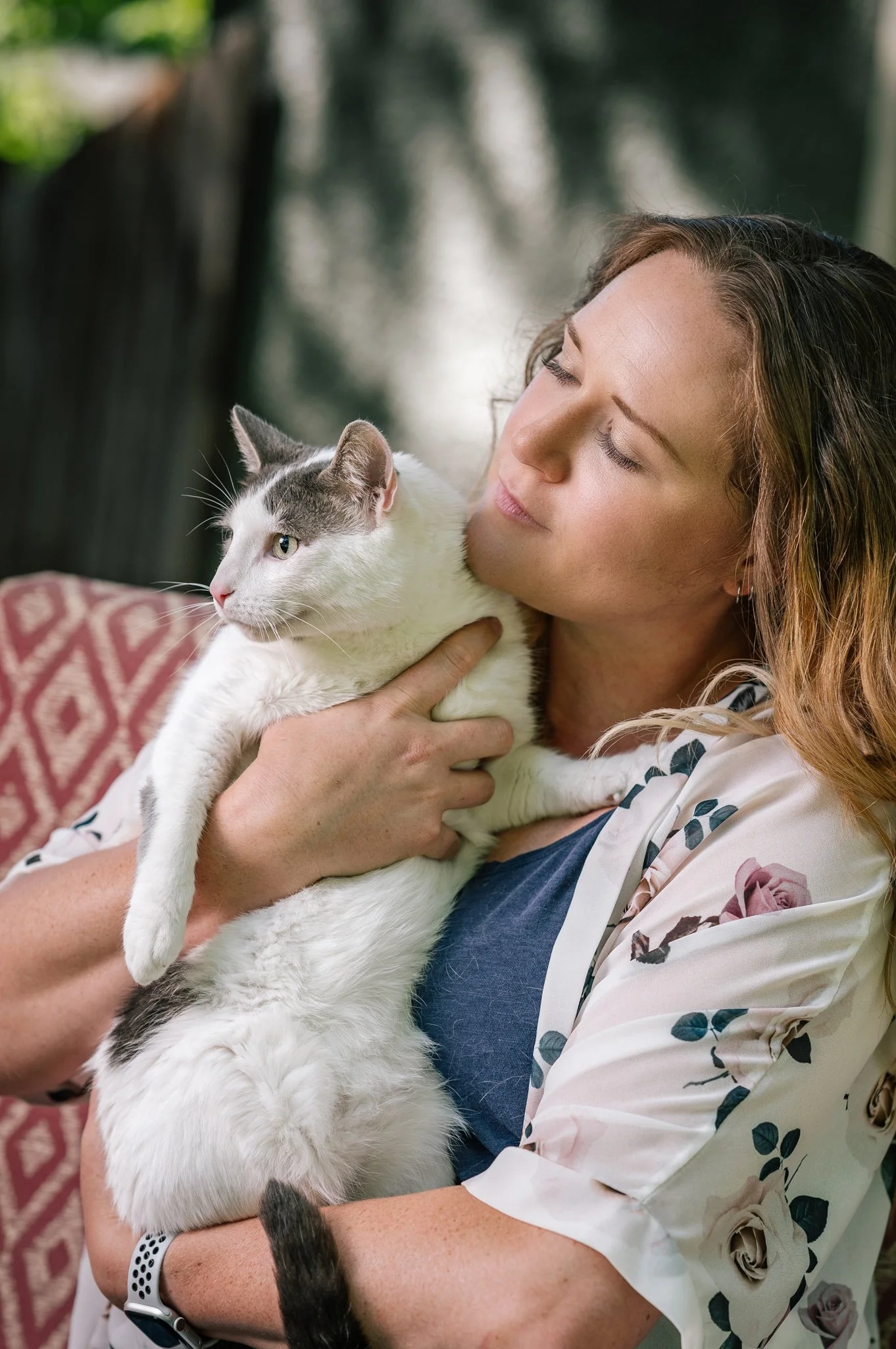 A woman holding a white and gray cat close to her face indoors.
