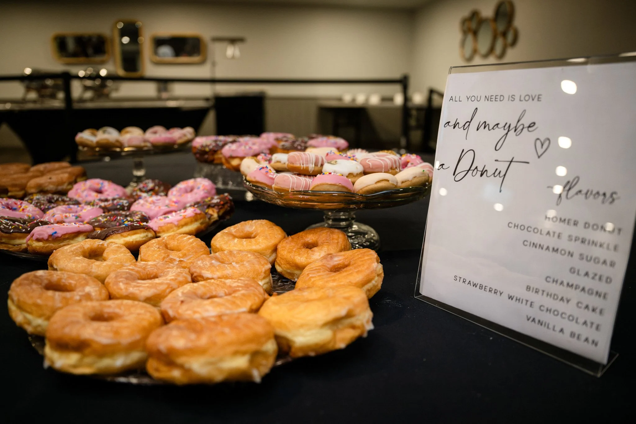 Assorted donuts with pink, white, and chocolate frosting and sprinkles on display at a dessert table.