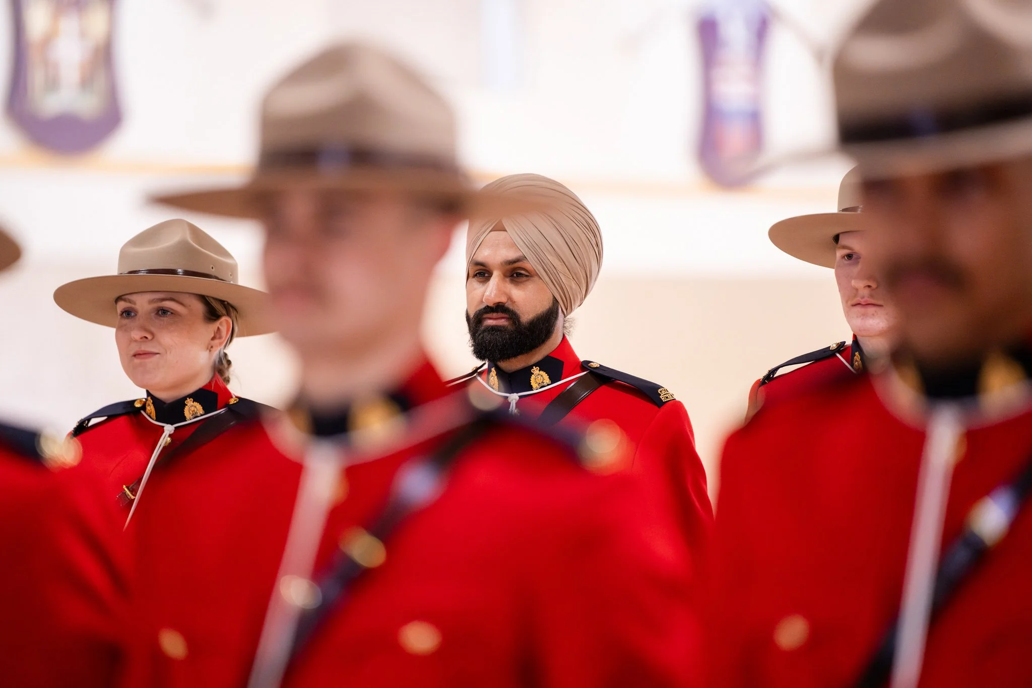 Group of Mountie officers in red uniforms and tan hats during a formal ceremony, with one man wearing a turban.