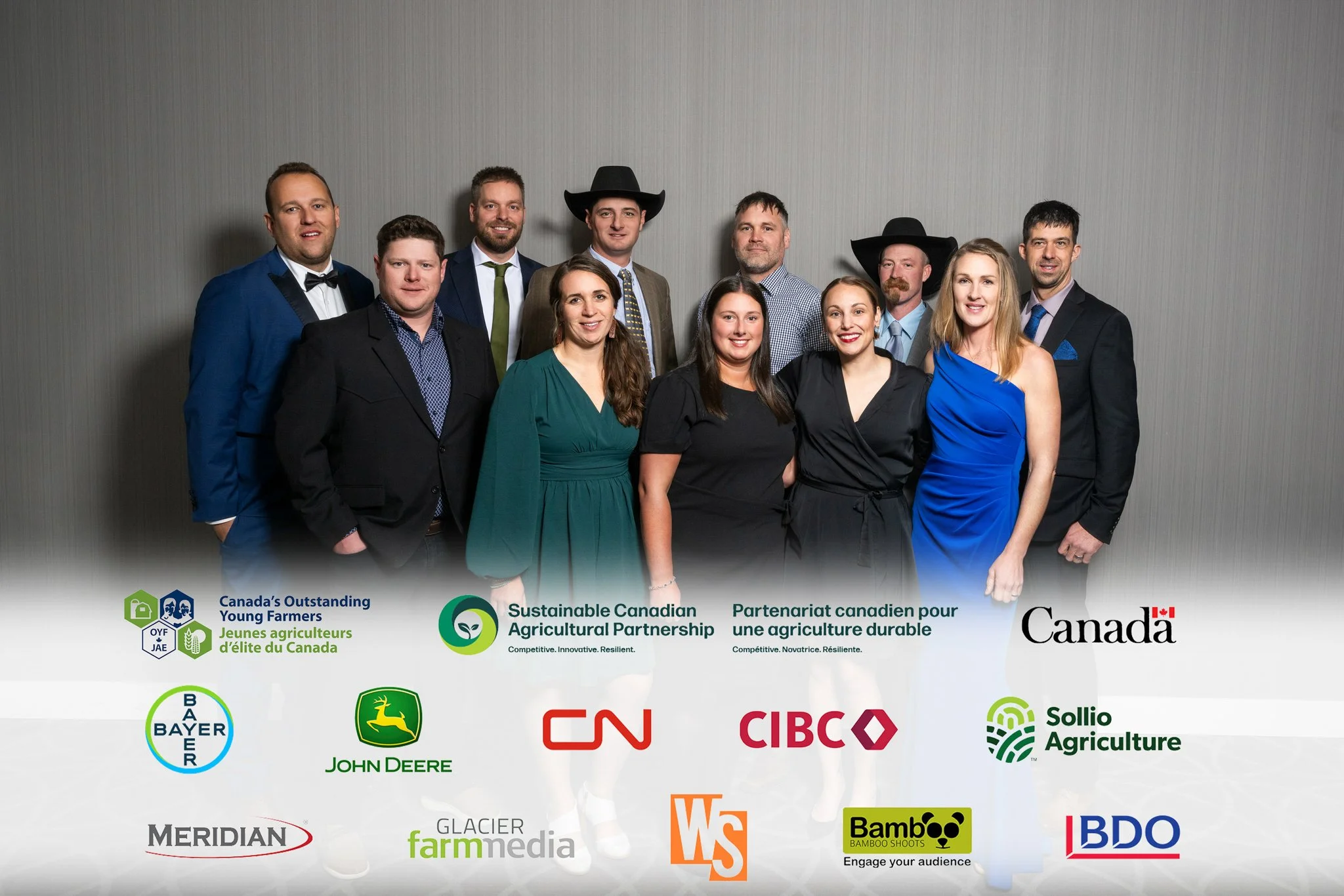 A group of twelve people dressed in formal attire posing for a photo at an event, standing in front of a gray wall, with logos of various agricultural organizations and companies displayed at the bottom.